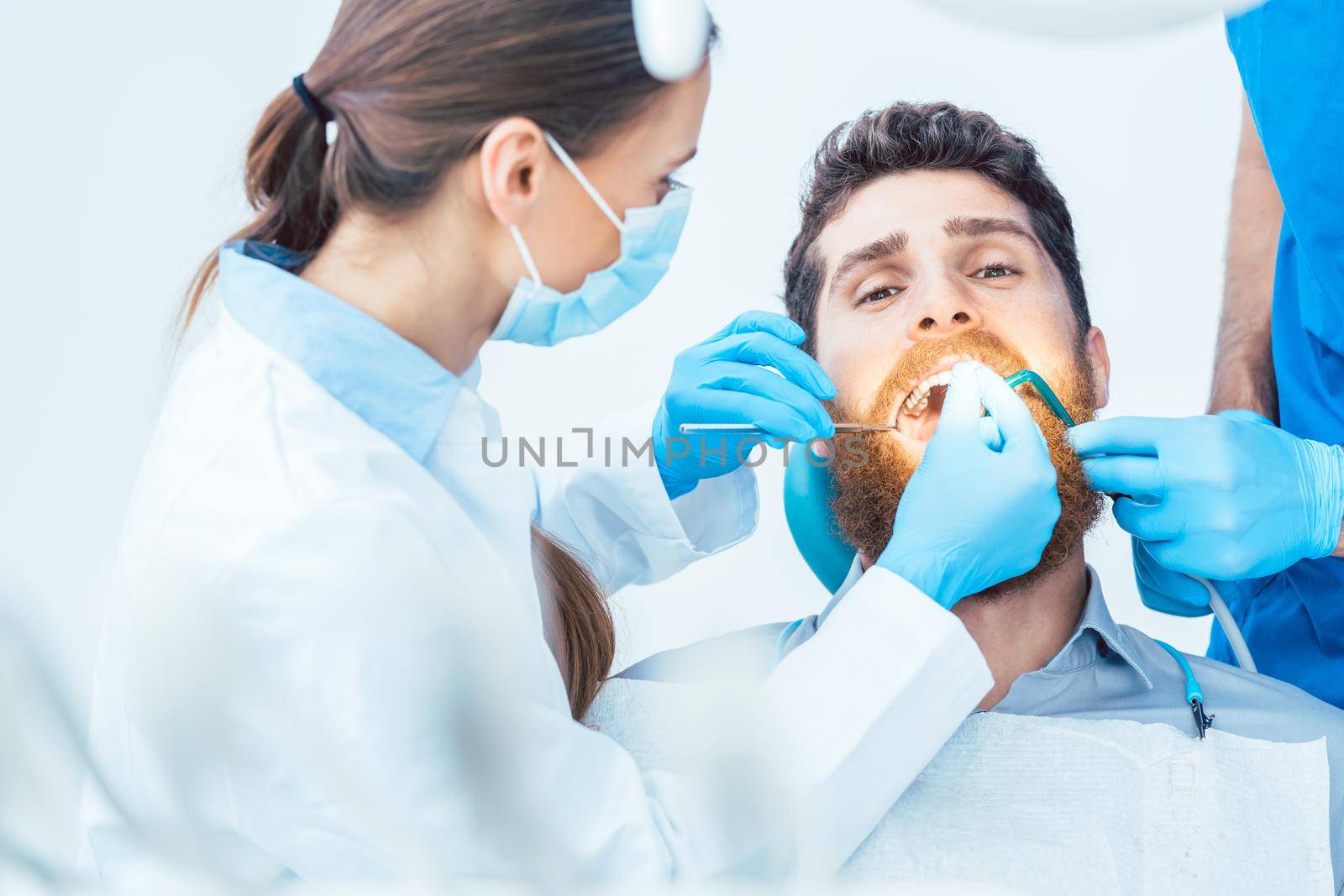 Young man during a painless oral procedure in the dental office by Kzenon