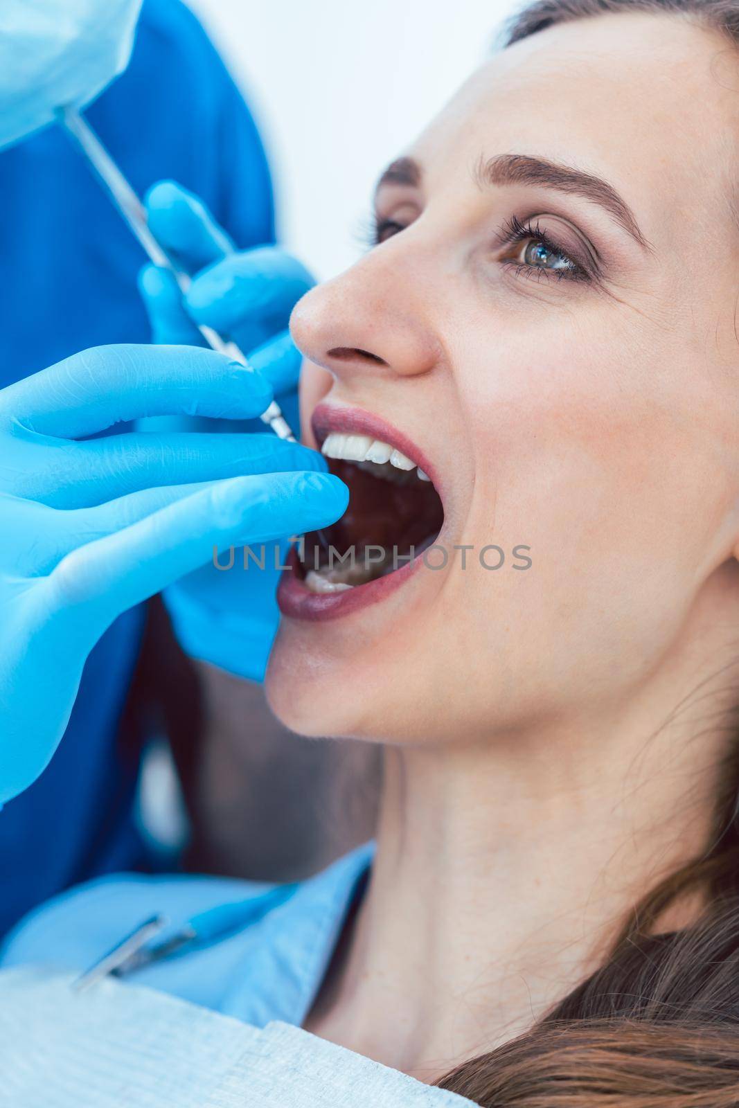 Close-up of the hands of a dentist wearing surgical gloves and using sterile medical equipment, while cleaning the teeth of a young woman in a modern dental clinic