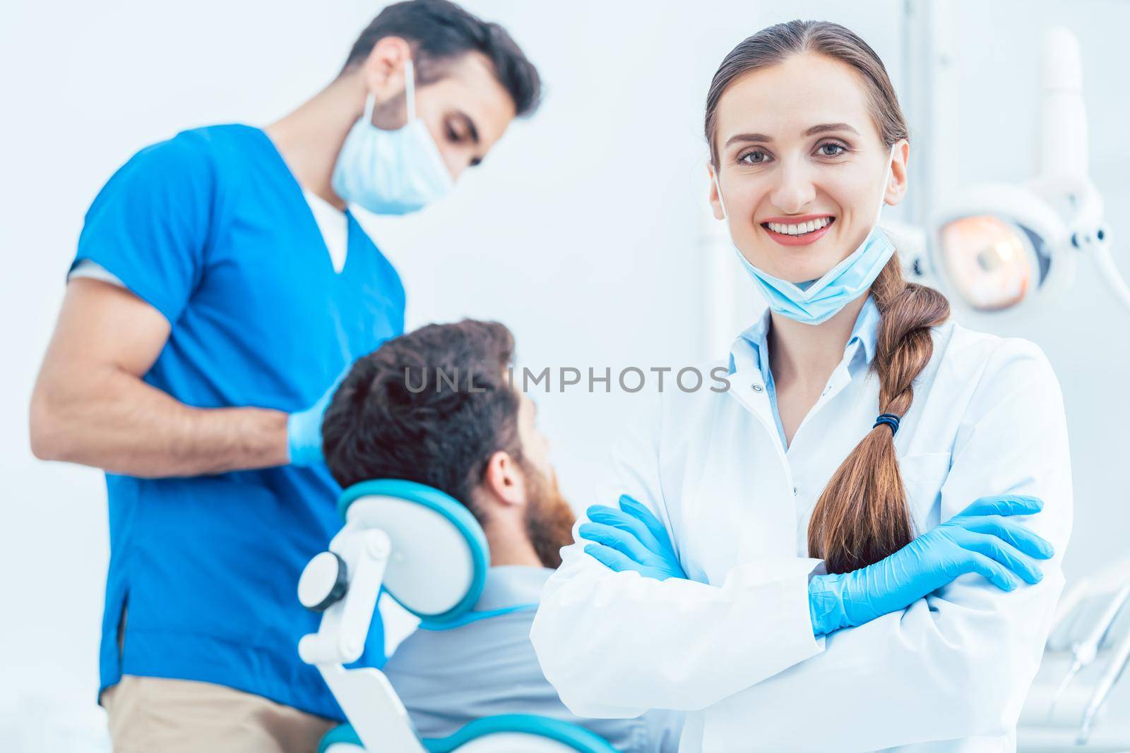 Portrait of a happy and confident female dentist wearing sterile white coat and surgical gloves, while looking at camera in the dental office of a modern clinic with reliable specialists