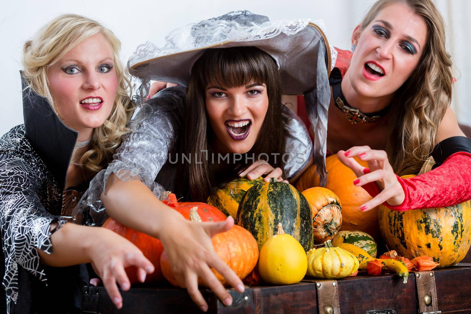 Four cheerful beautiful women toasting while celebrating Halloween together during costume party indoors in a decorated room