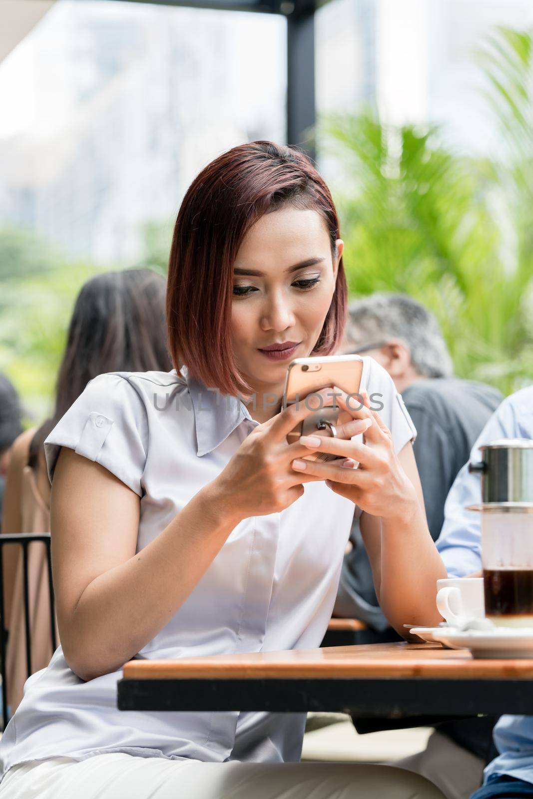 Portrait of a young Asian woman smiling while using a mobile phone connected to the internet outdoors at a coffee shop