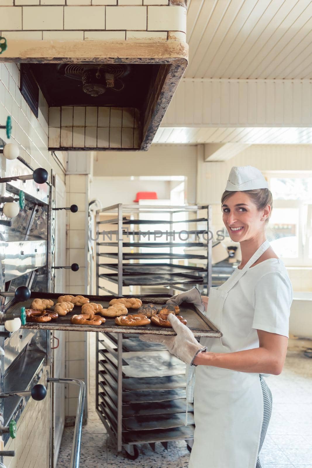 Baker woman getting bakery products out of oven on baking sheet