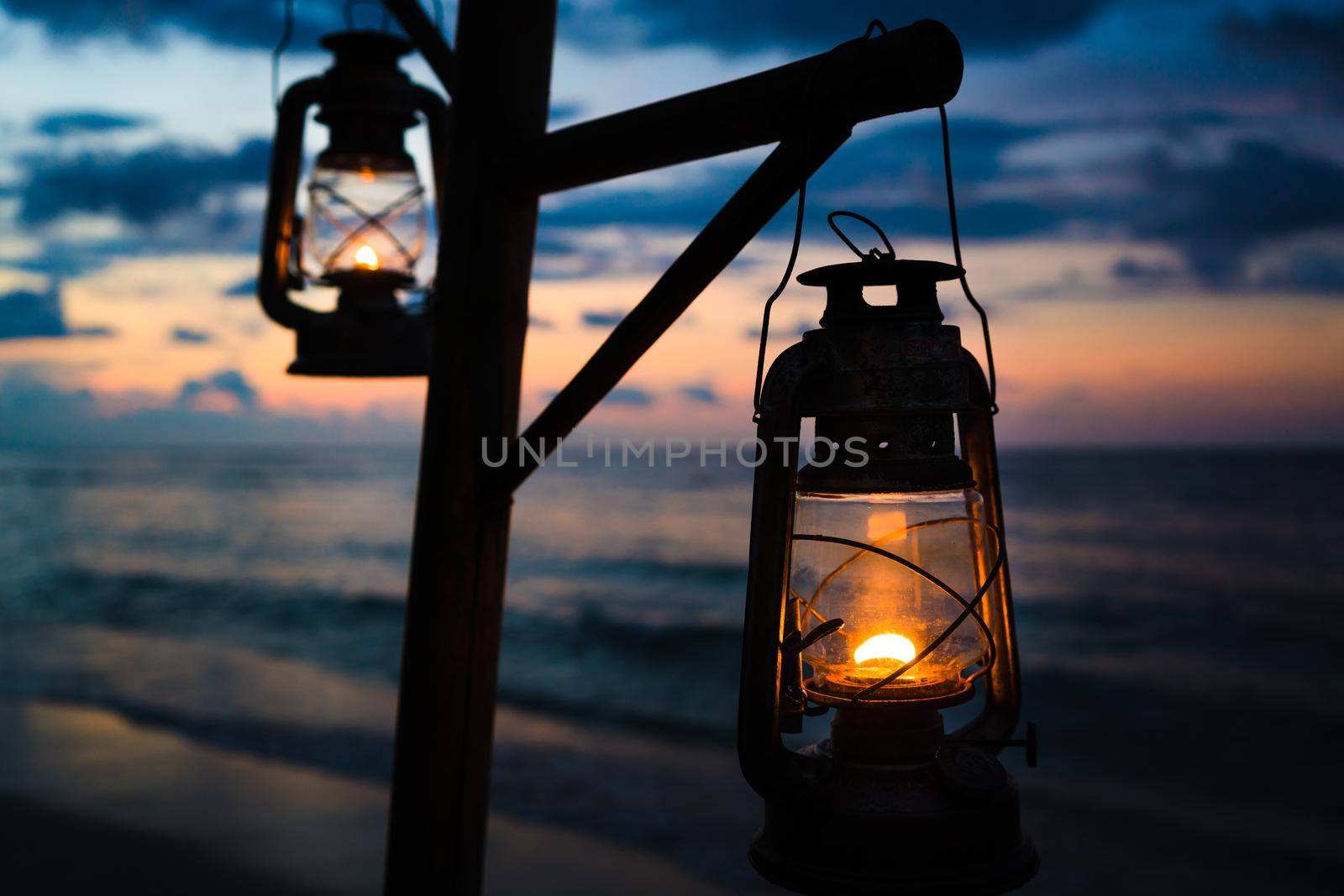 Sunset on an island beach with lanterns illuminating the scene by Kzenon