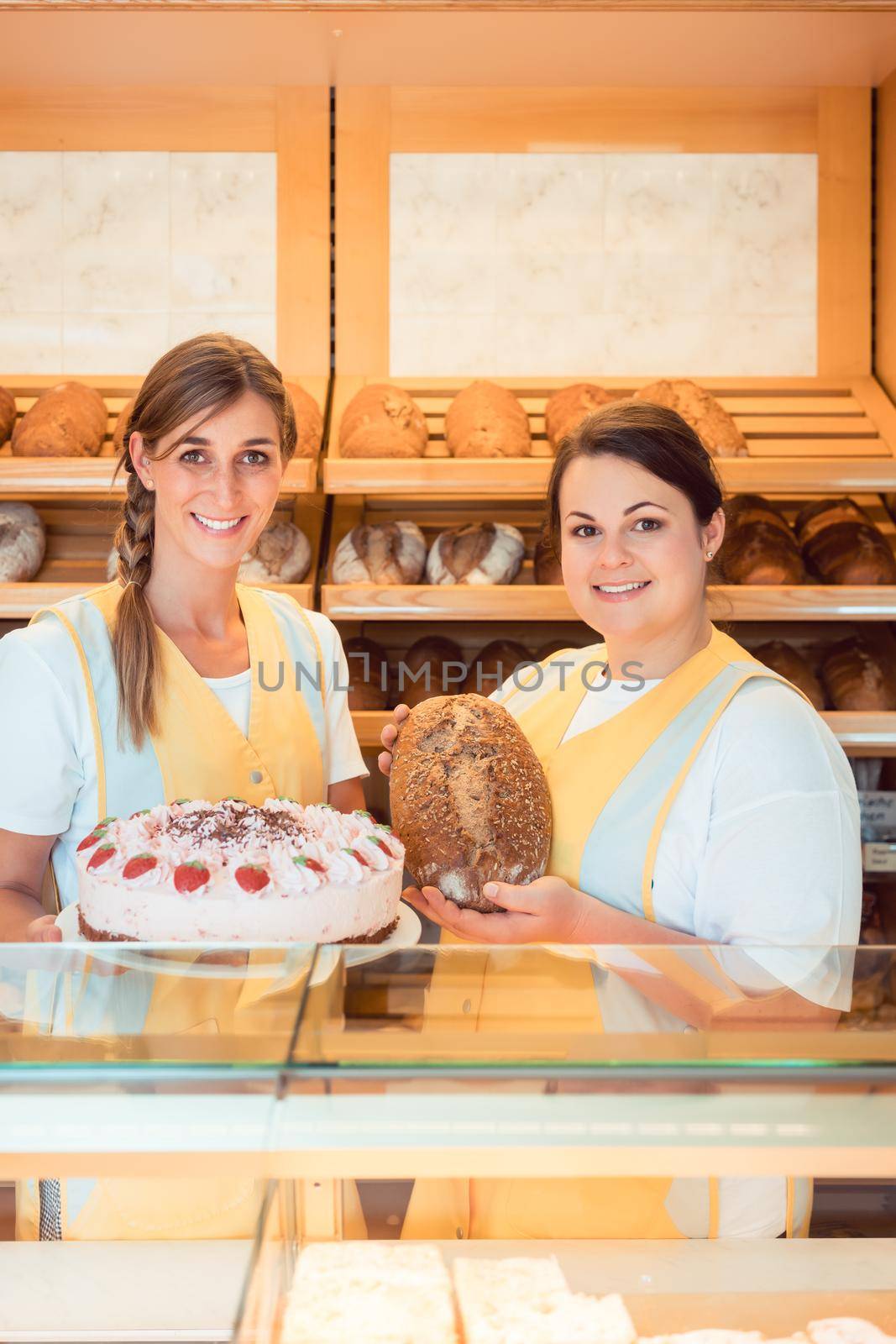 Sales women in bakery with cake and bread showing them to the customer