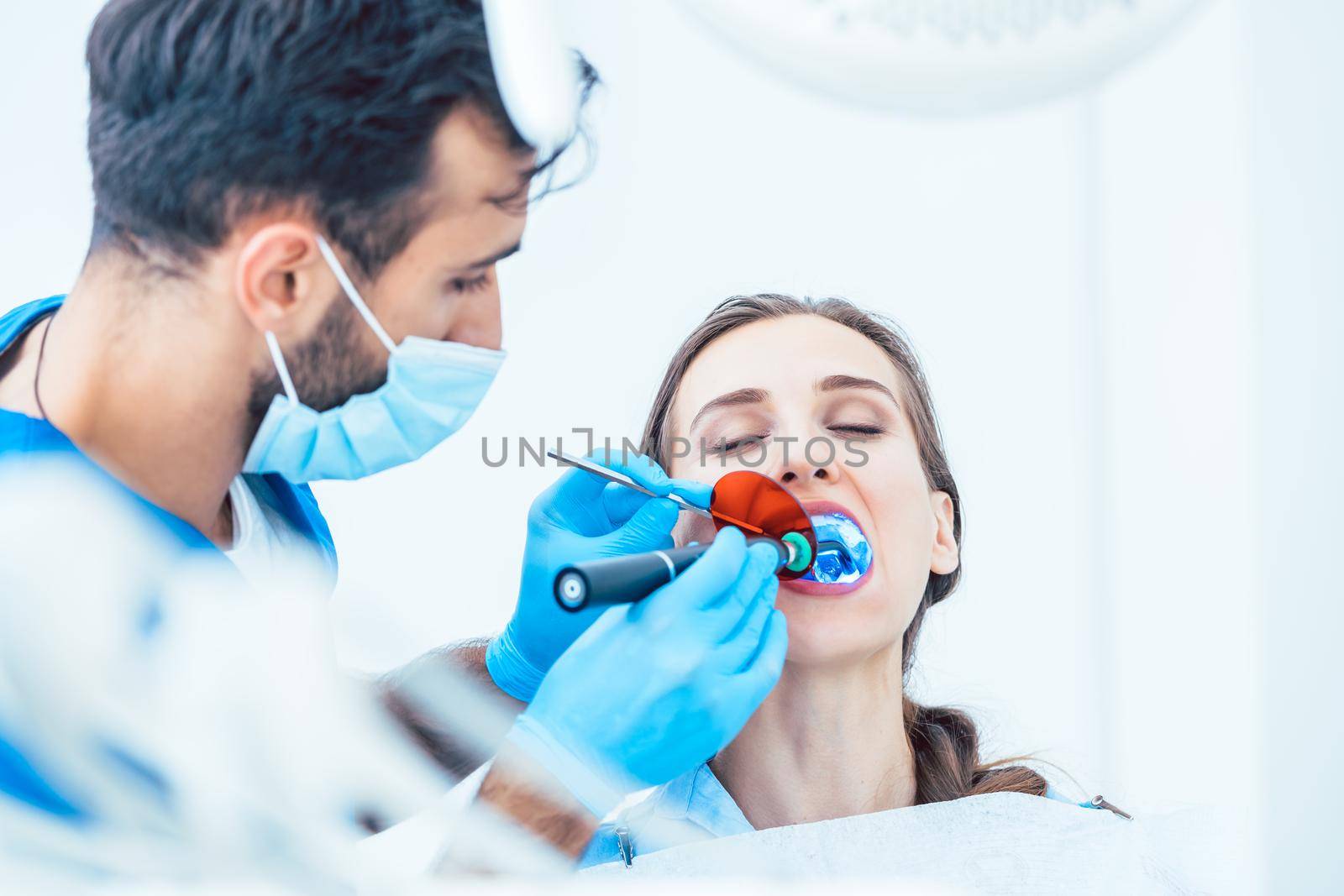 Young woman during innovative oral treatment with cordless LED curing light machine for whitening and restoration in the dental office of an experienced dentist