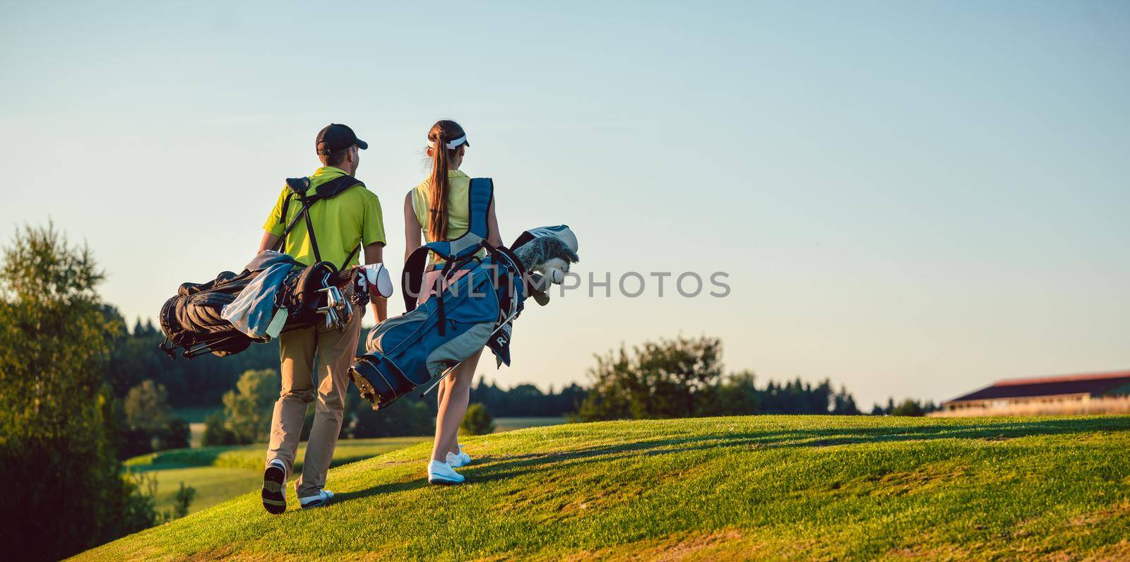 Happy couple wearing golf outfits while carrying stand bags by Kzenon