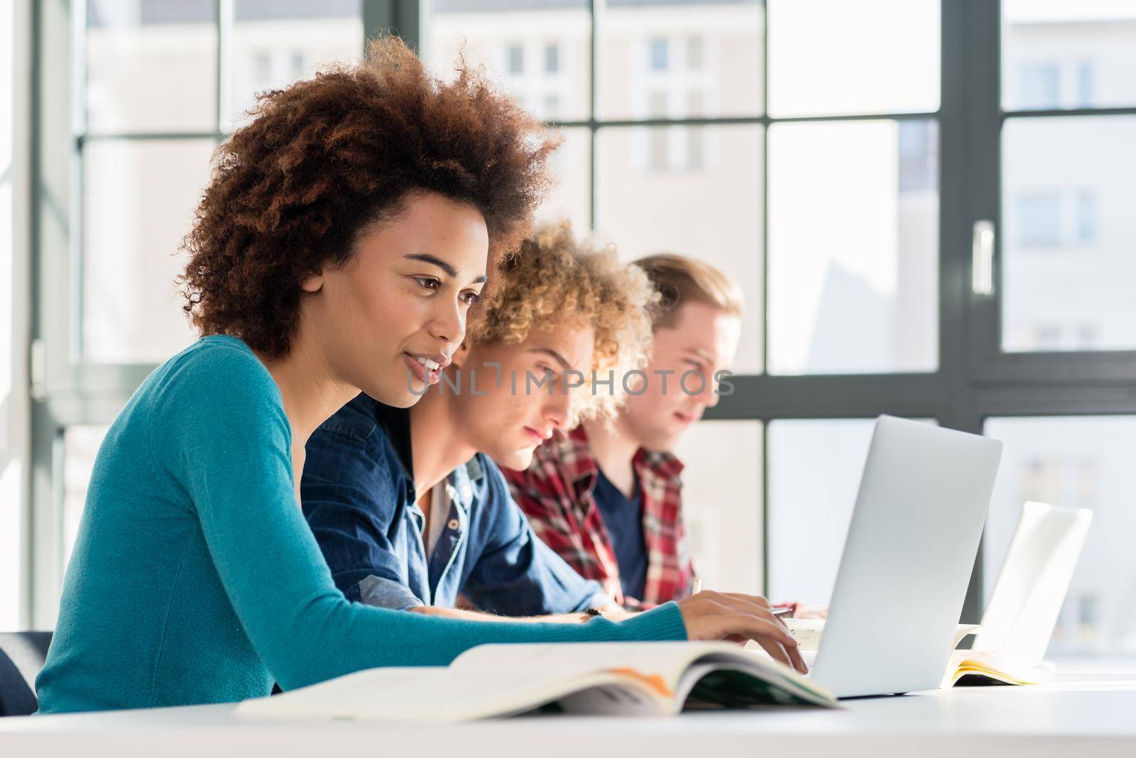 Side view of a happy student smiling while using a laptop for online information or virtual communication through social media during class at the university