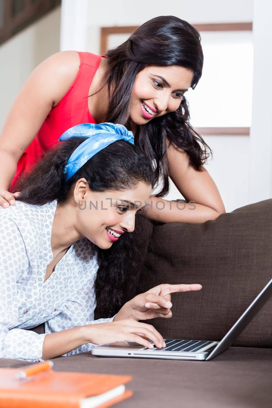 Two young women smiling while browsing the internet on laptop indoors at home