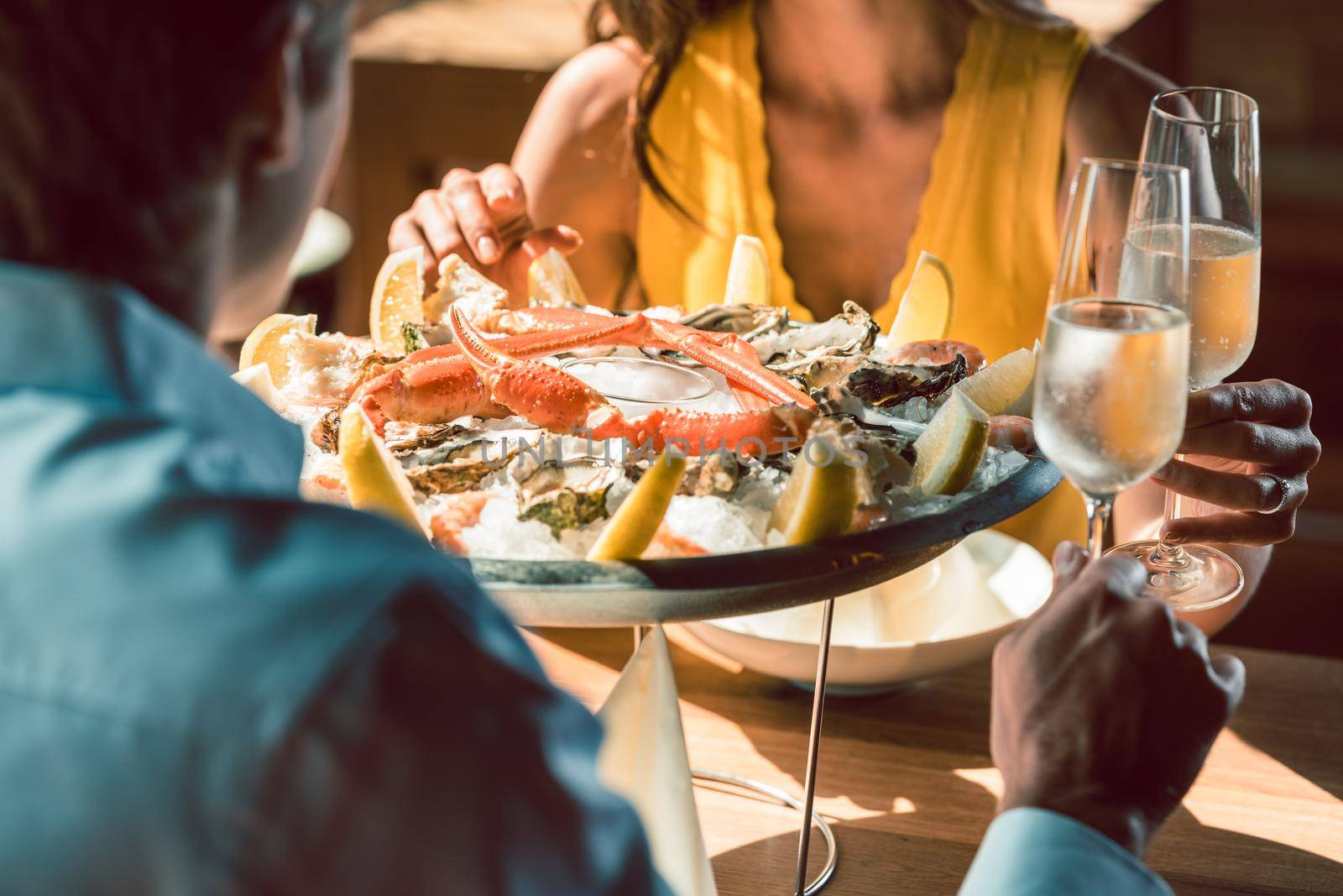 Close-up of fresh oysters and crabs served on ice with lemon at the table of a romantic couple in love, celebrating with champagne at a trendy restaurant