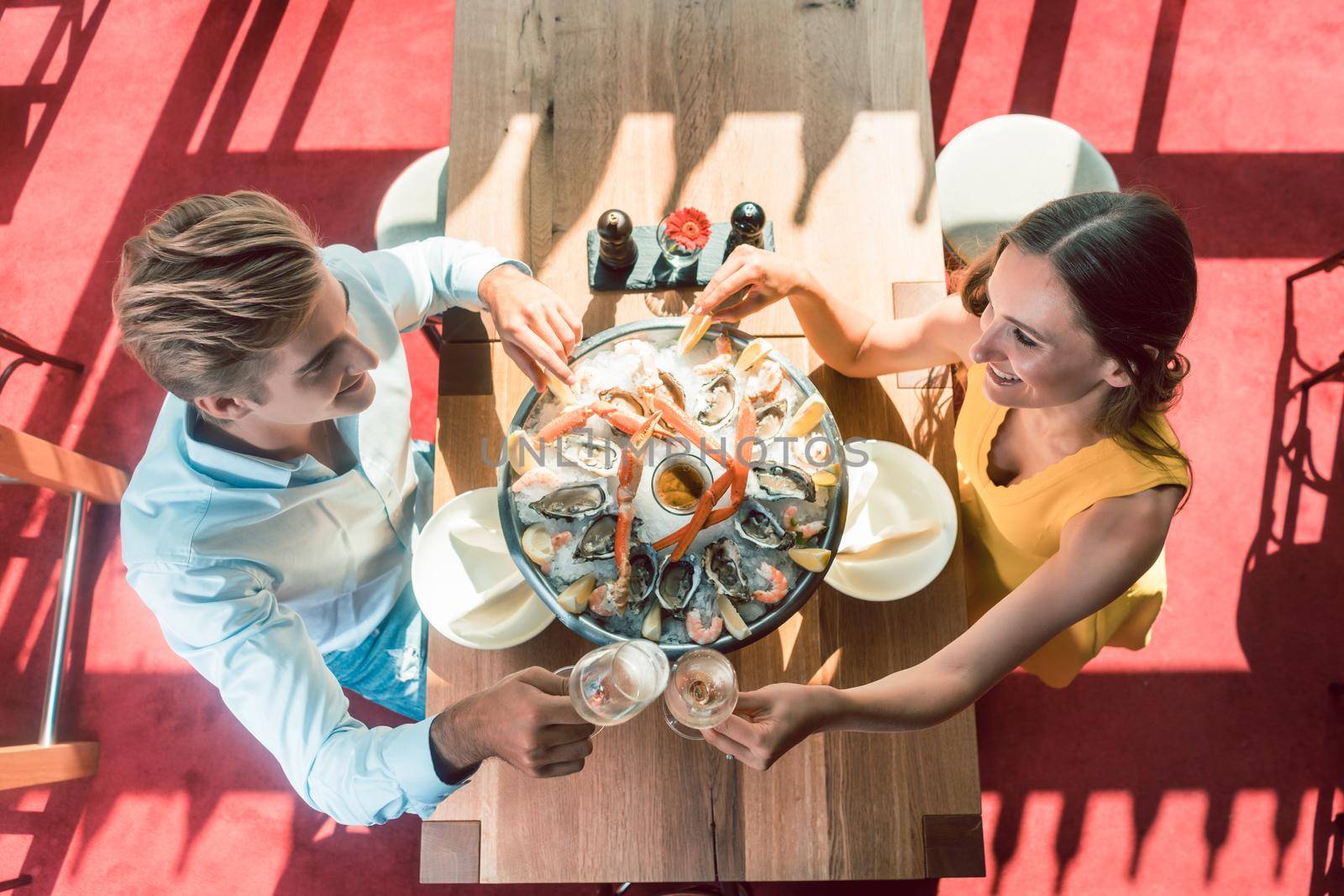 High-angle view of a happy young couple toasting with champagne during romantic dinner with fresh seafood at a trendy restaurant