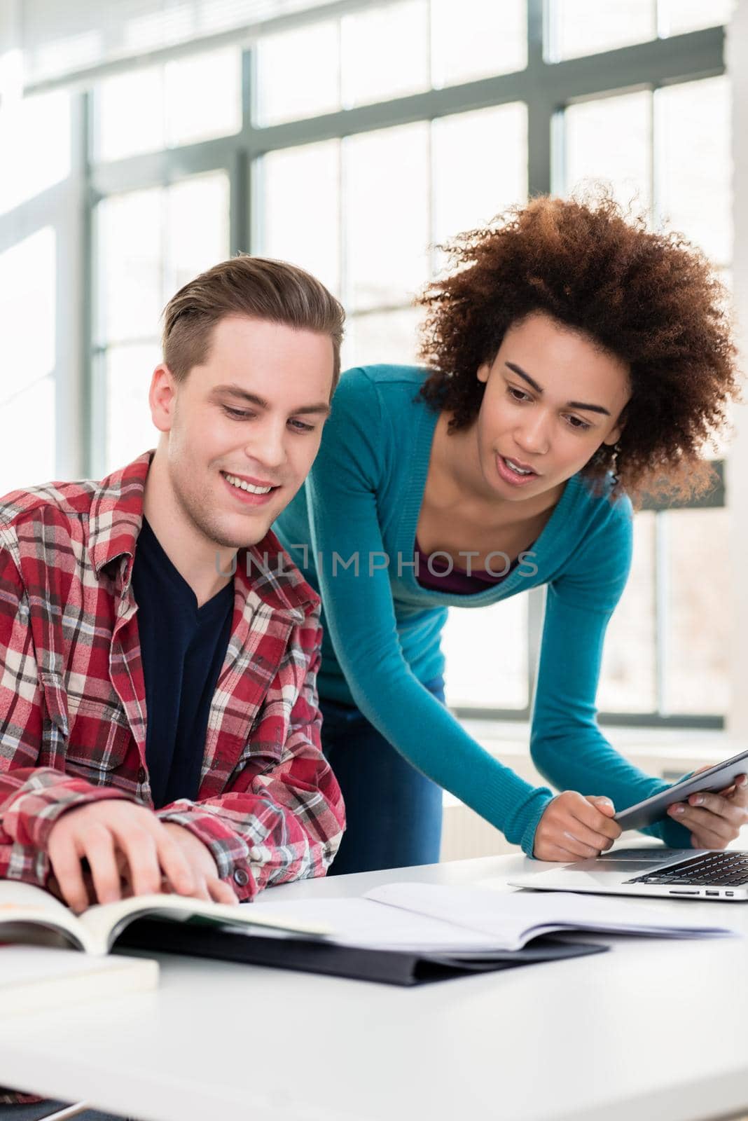 Two young students browsing internet for online useful up-to-date information while writing together an assignment in the interior of a modern university