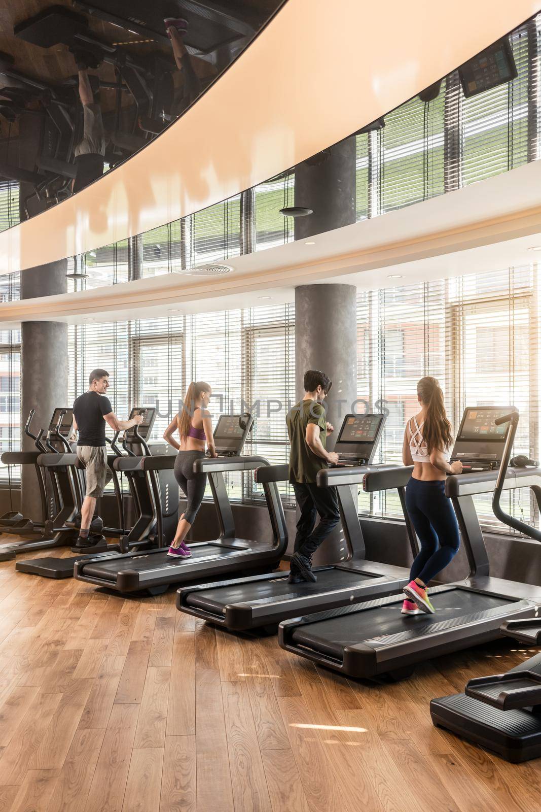 Group of four people, men and women, running on treadmills in modern and luminous fitness gym