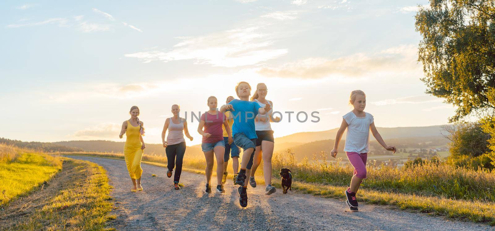 Playful family running and playing on a path in backlit summer landscape