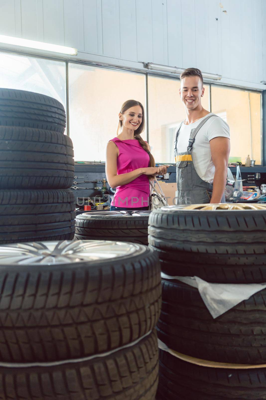 Handsome auto mechanic helping a female customer to choose from various high-quality tires in a contemporary automobile repair shop