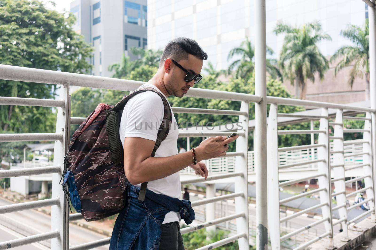 Young tourist using the mobile phone for communication or useful online information while walking on a pedestrian bridge in Indonesia