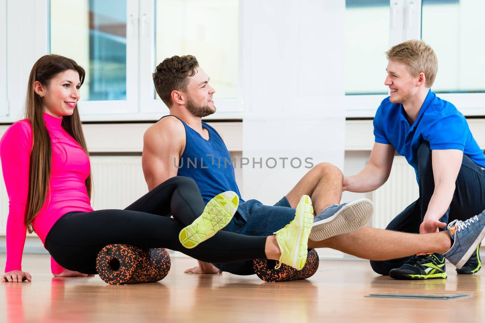 Man and woman with physiotherapist at gym doing floor gymnastics with roll
