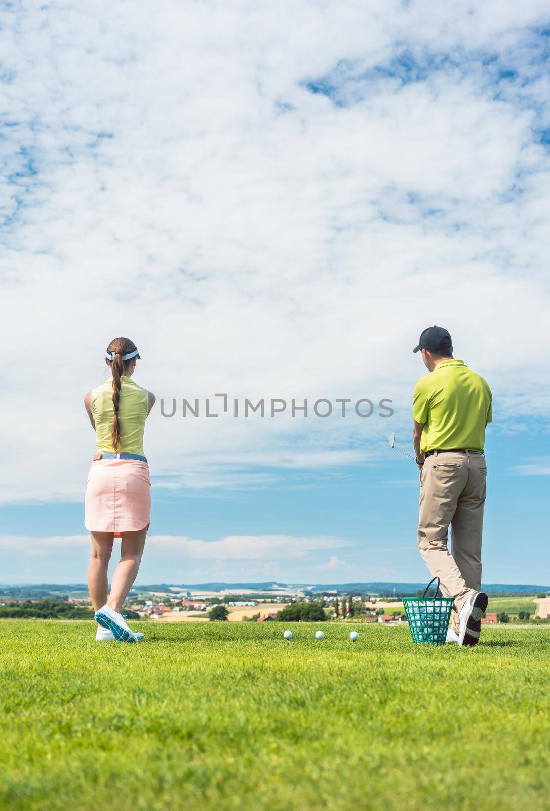 Full length of a young woman smiling while practicing the correct move for striking during golf class with a skilled professional player outdoors