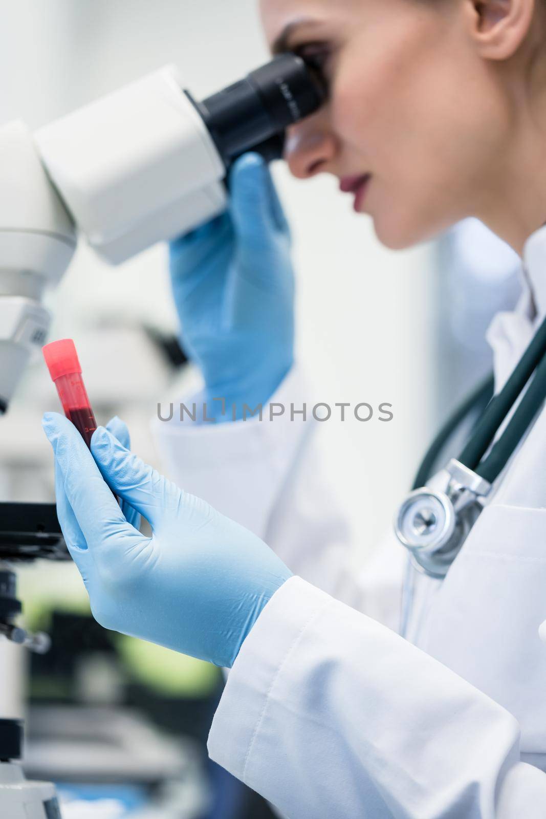 Woman examining blood sample under microscope in medical or scientific laboratory