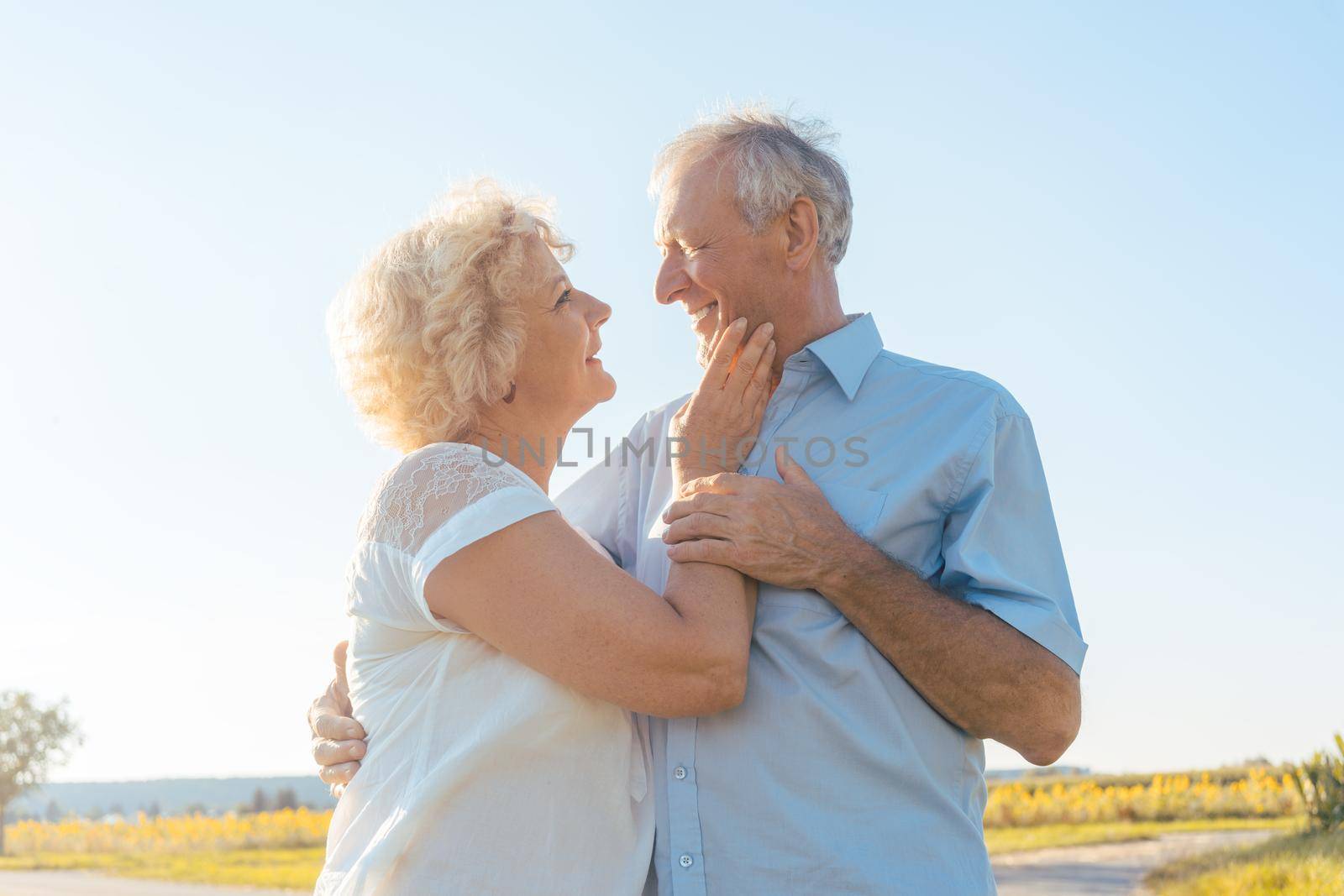 Low-angle view of a romantic elderly couple enjoying health and nature while standing together on a field in a sunny day of summer