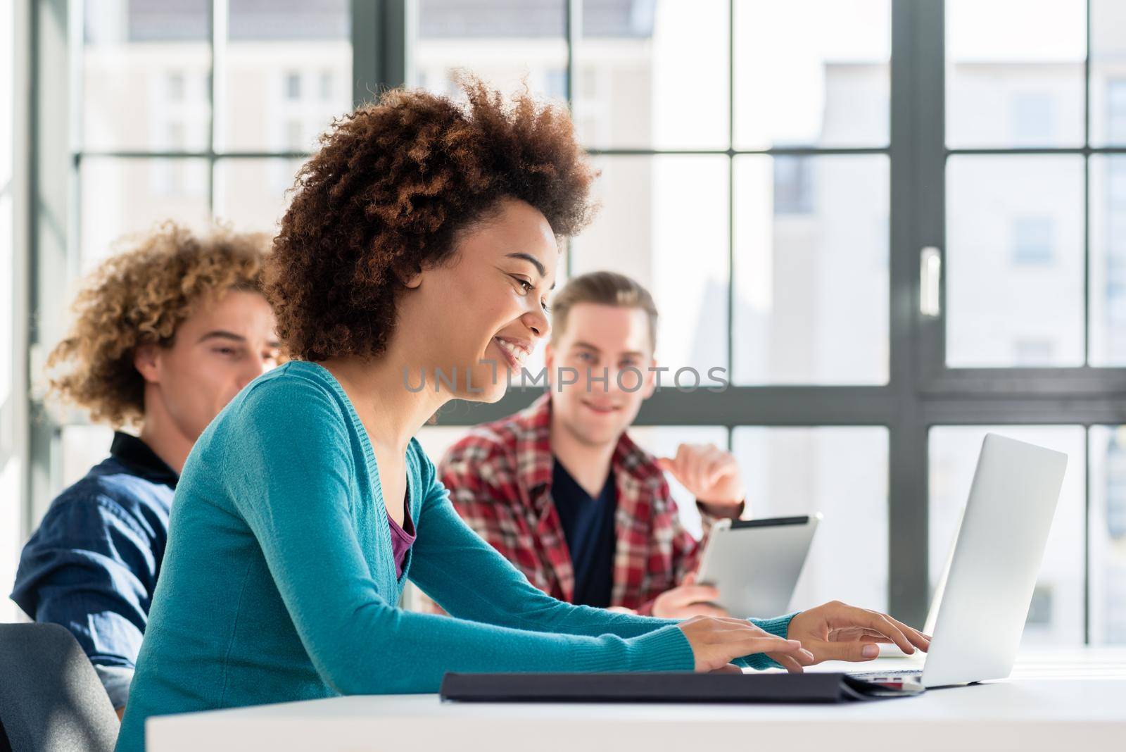 Side view of a happy student smiling while using a laptop for online information or virtual communication through social media during class at the university