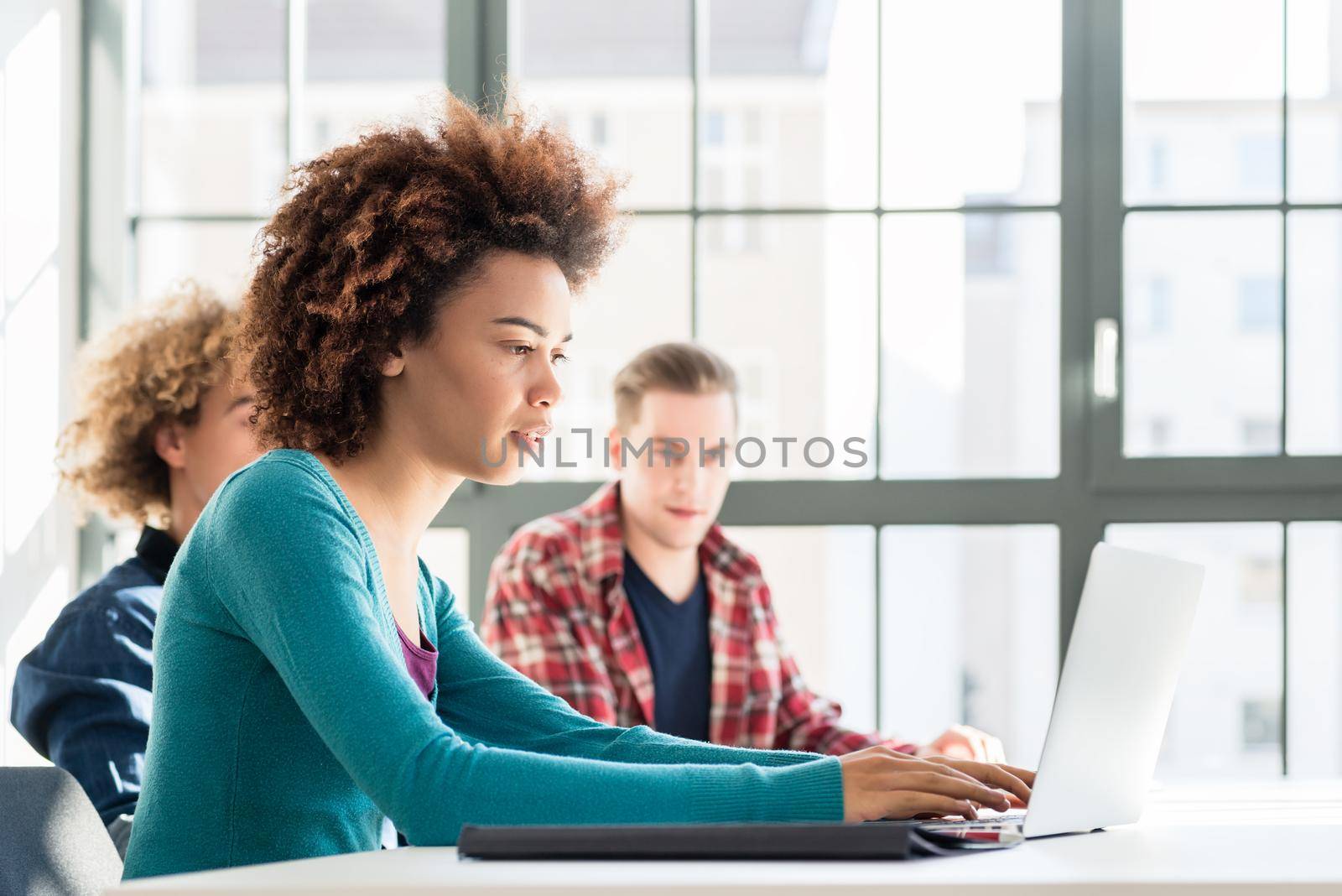 Side view of a happy student smiling while using a laptop for online information or virtual communication through social media during class at the university