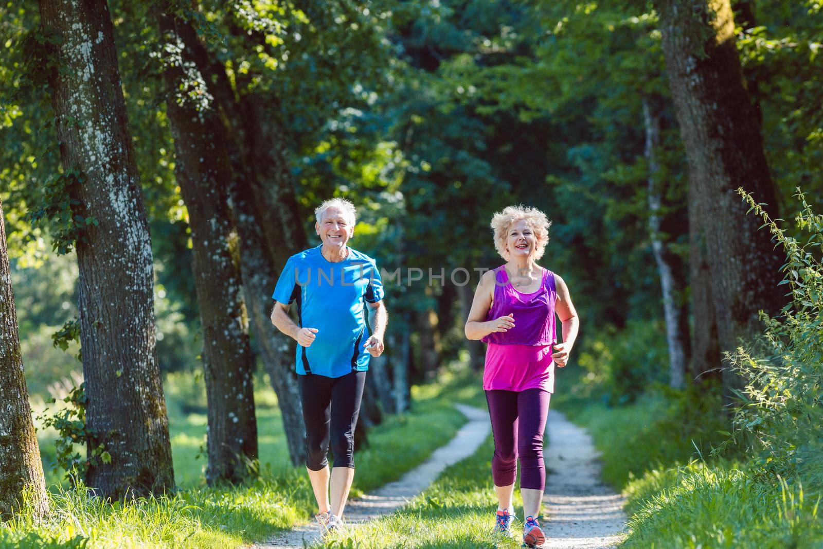 Full length front view of two active seniors with a healthy lifestyle smiling while jogging together outdoors in the park