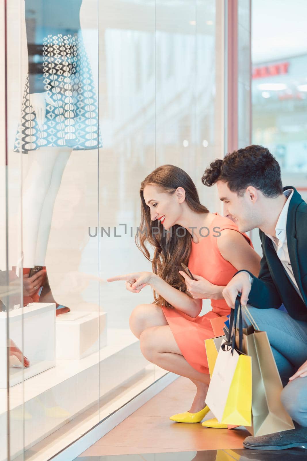 Woman and man looking at fashion shop window wanting to buy a dress