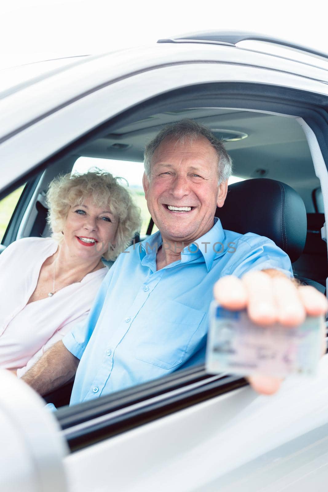 Portrait of a happy senior man showing his available driving license while sitting in the car next to his cheerful wife