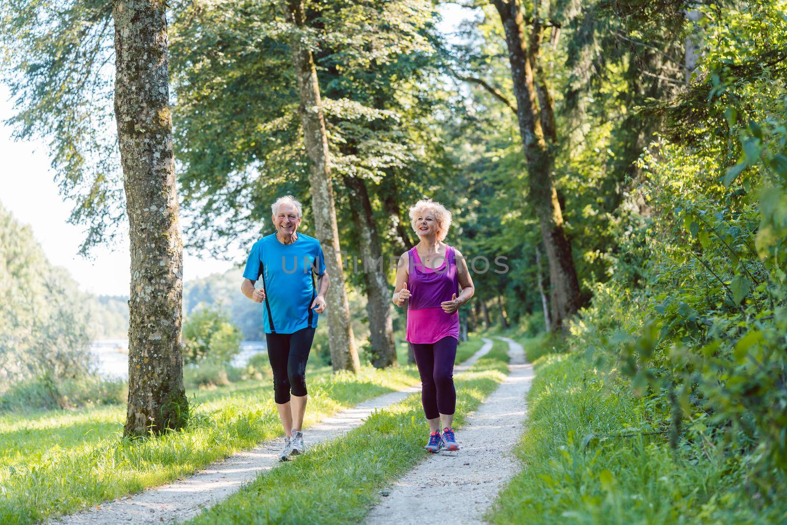 Full length front view of two active seniors with a healthy lifestyle smiling while jogging together outdoors in the park