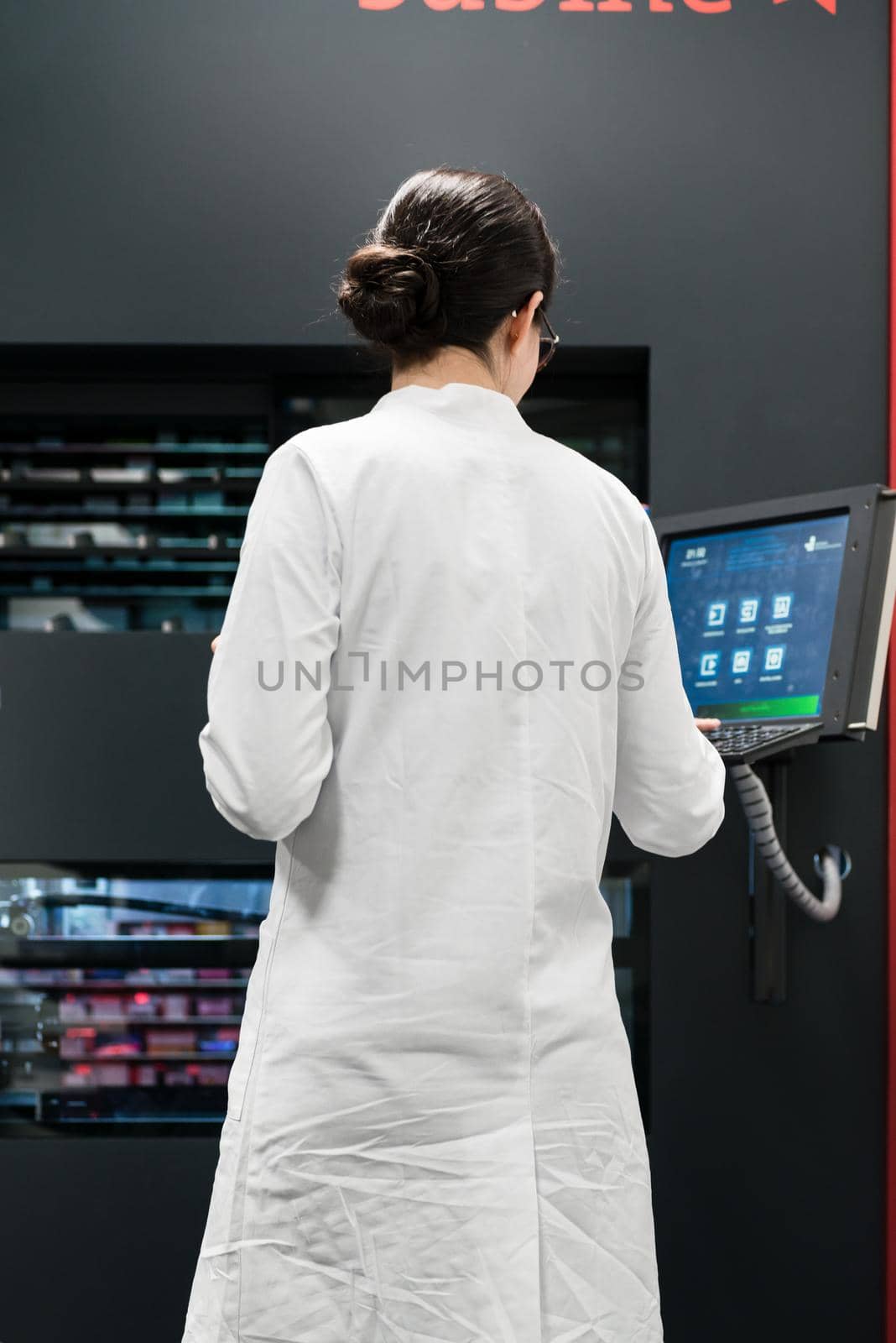 Low-angle rear view of an experienced female pharmacist using a computer while managing the drug stock in a contemporary pharmacy with modern technology
