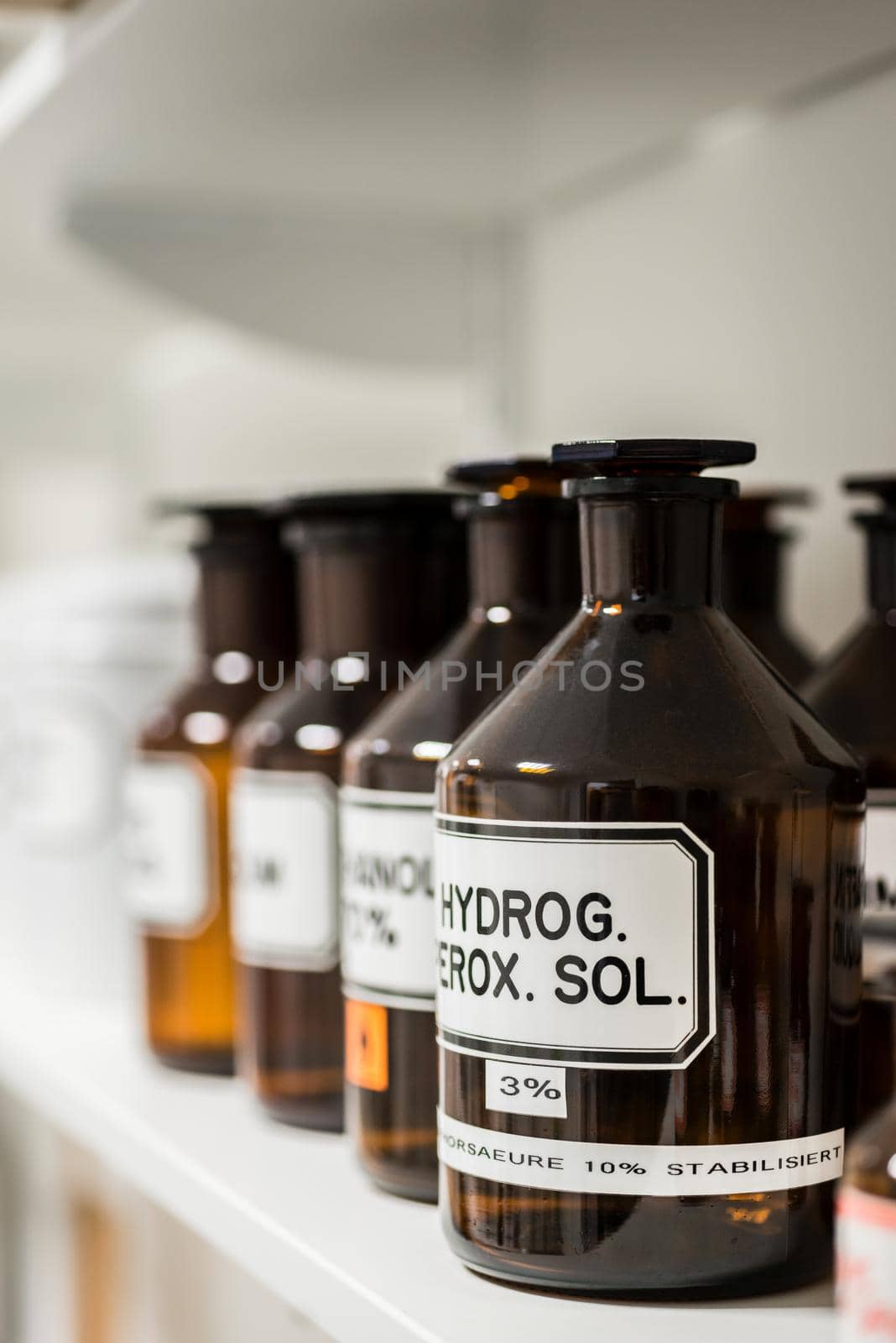 Close-up of the labeled glass container of a chemical pharmaceutical substance on a shelf, next to various supplies in the storage of a modern drugstore
