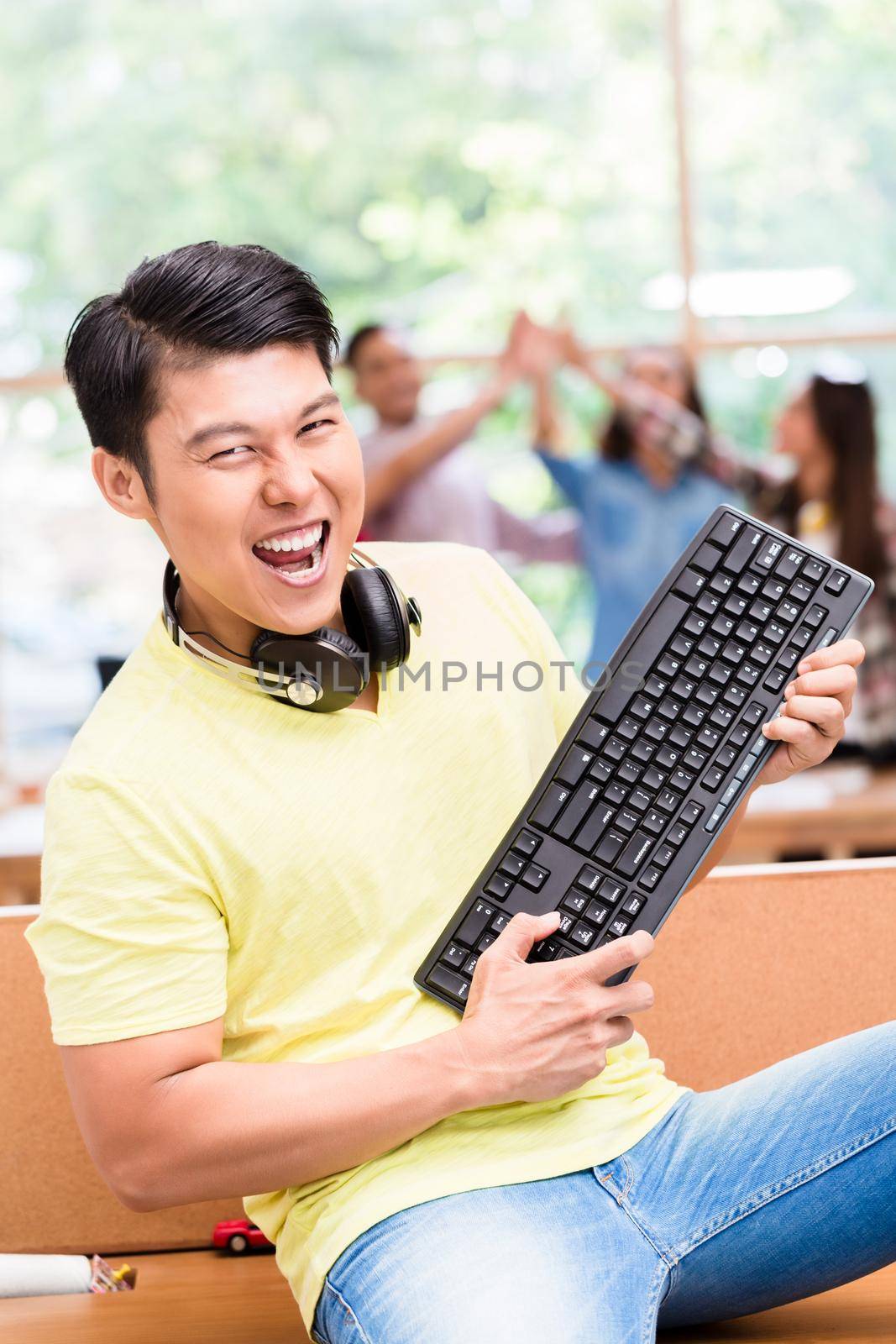 Young Chinese employee happy for his successful work on computer by Kzenon