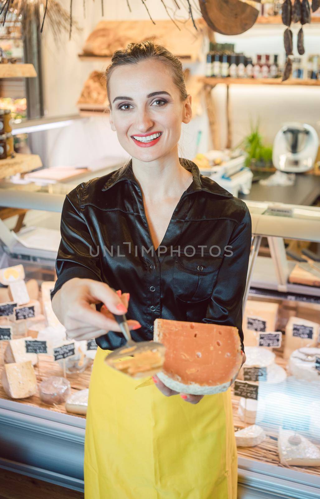 Beautiful woman offering cheese on delicatessen counter cutting a test bit off