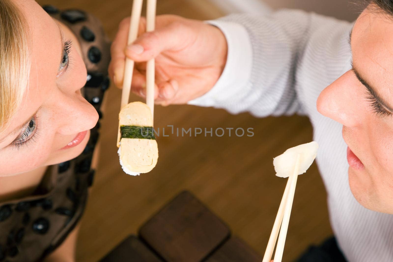 Couple feeding each other with sushi for dinner, romantic setting, presumably this is an advanced date; shallow focus on eyes