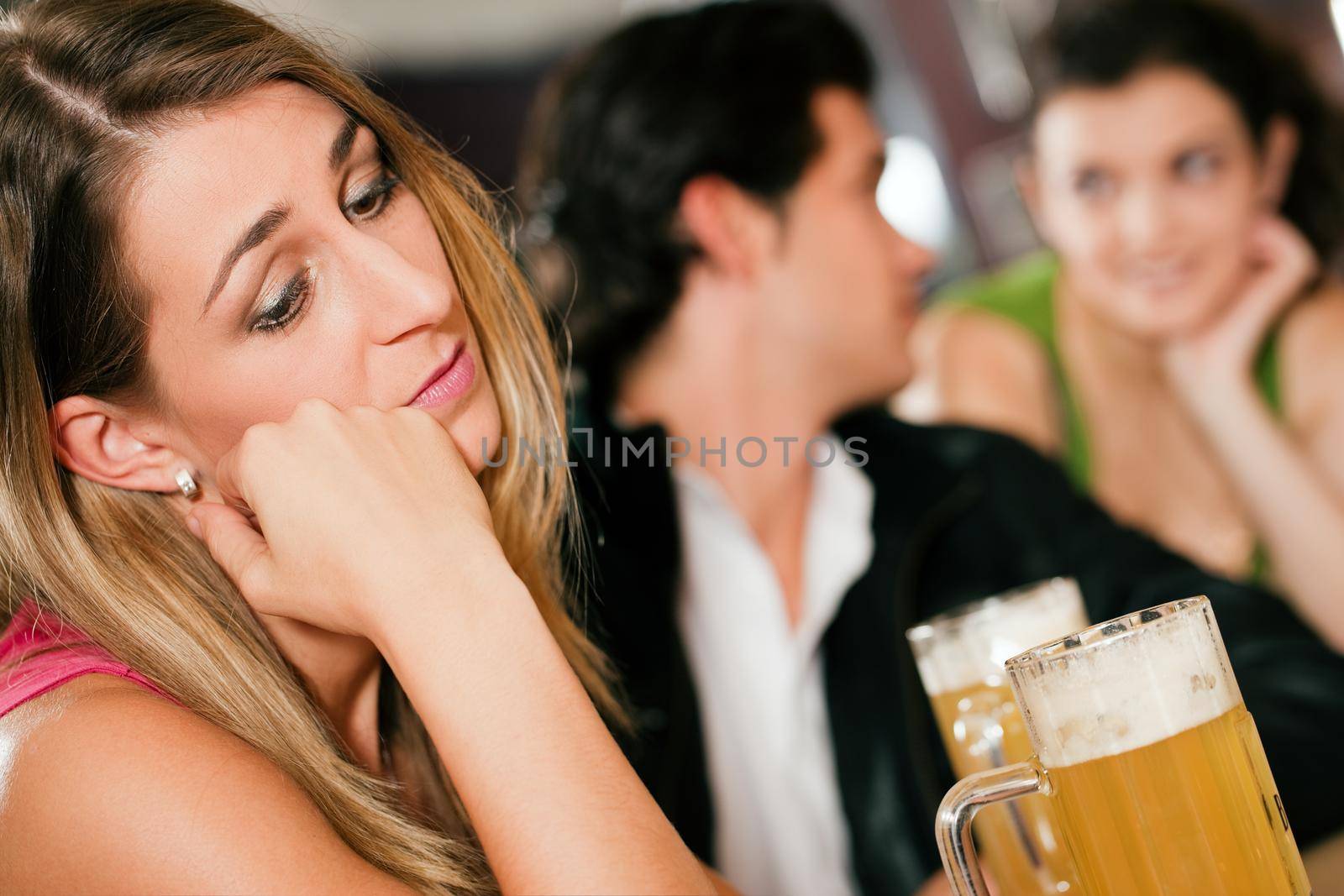 Group of people in a bar or restaurant drinking beer, woman in front being sad since her boyfriend is flirting with another girl dumping her