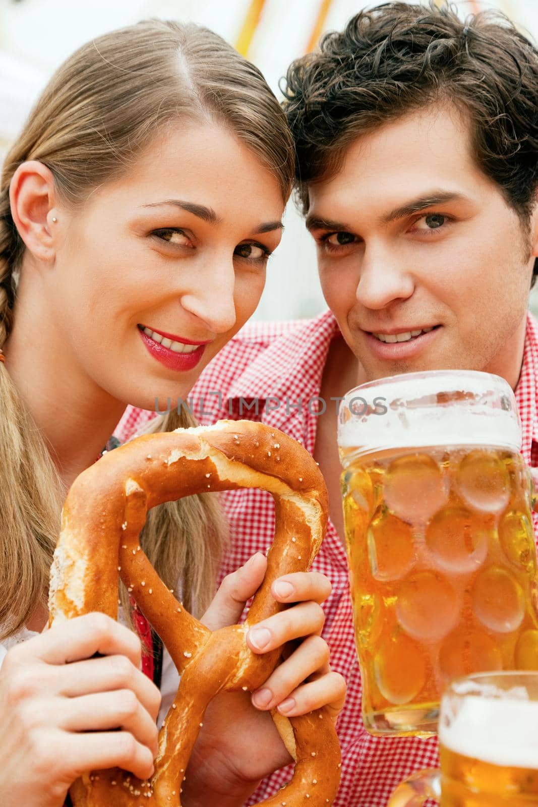 Couple in traditional German costume in a beer tent, he is having a drink, she a pretzel, scene could be located at the Oktoberfest or any Dult