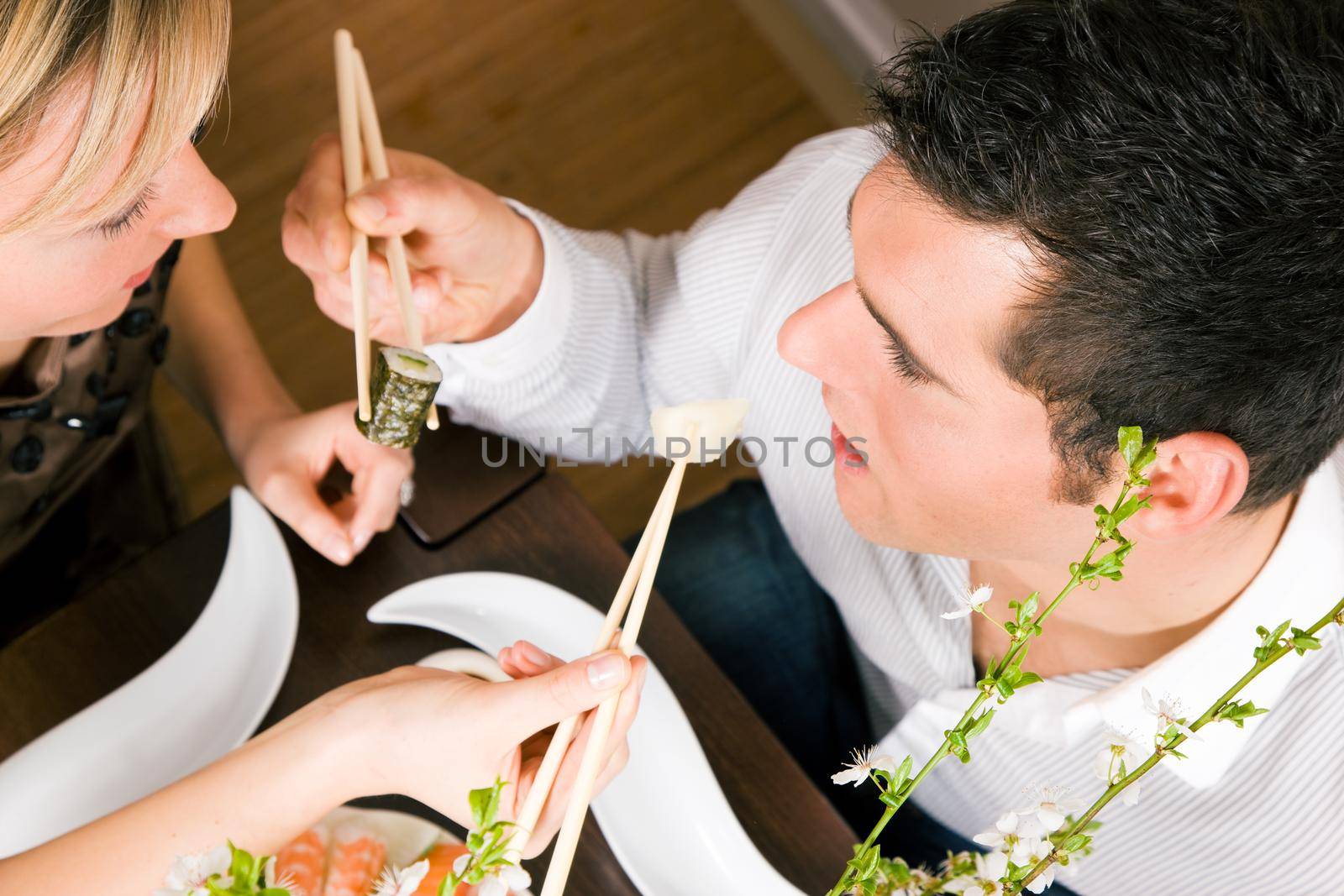 Couple feeding each other with sushi for dinner, romantic setting, presumably this is an advanced date; shallow focus on eyes