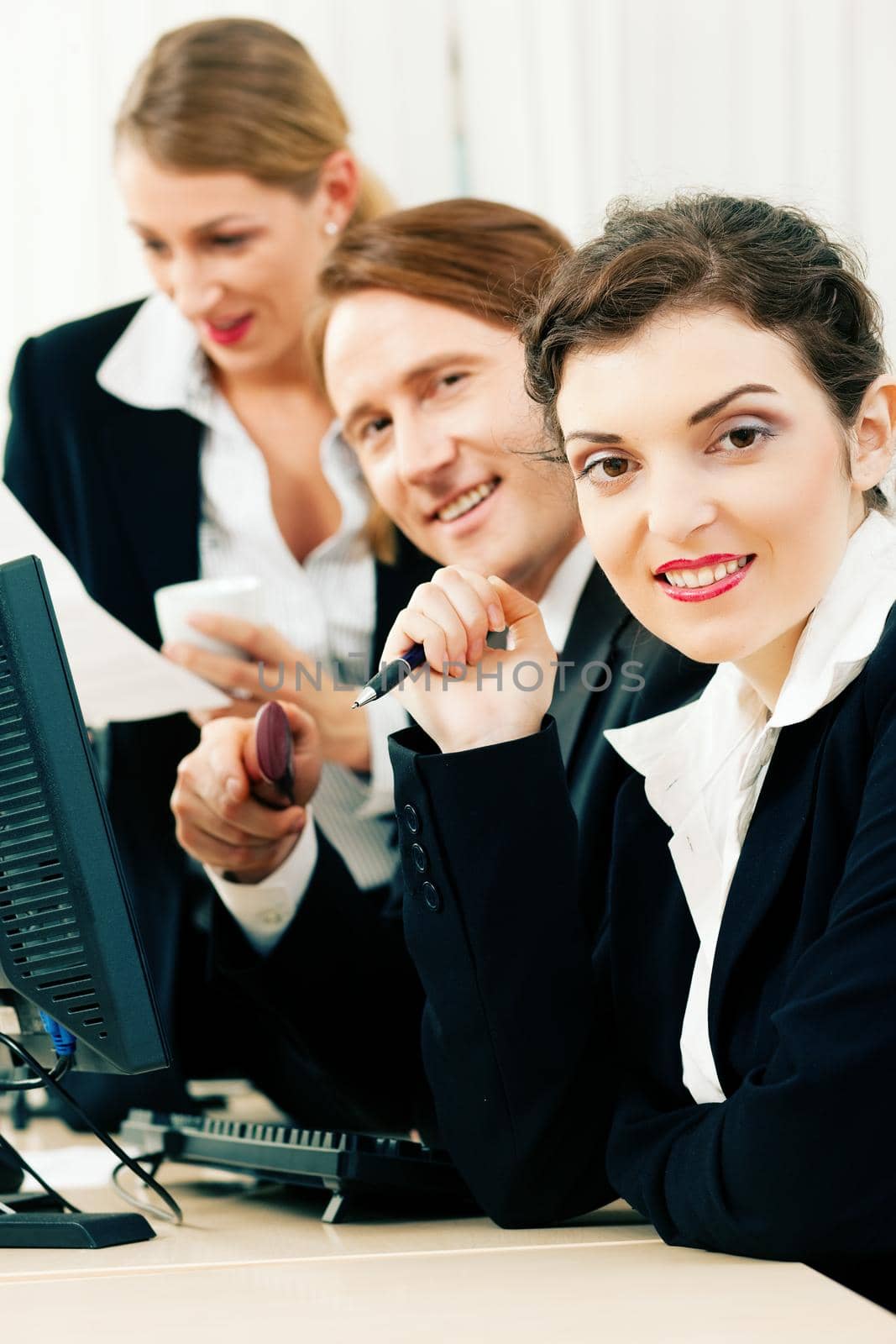 Small business team - man and two women - working in the office looking on a computer screen, one woman drinking a mug of coffee