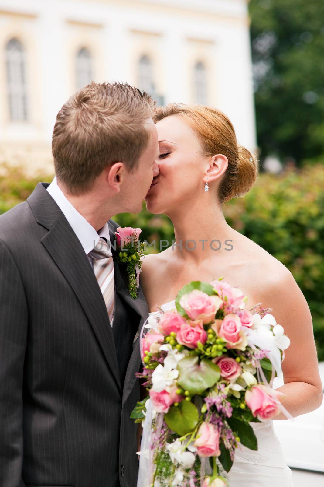 Wedding - groom kissing the bride in a park, she is holding the bouquet of flowers