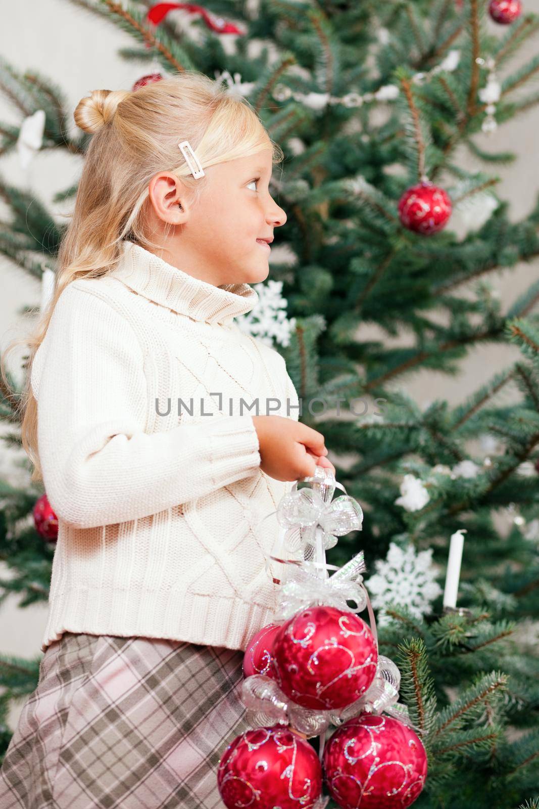 Young girl helping decorating the Christmas tree, holding some Christmas baubles in her hand