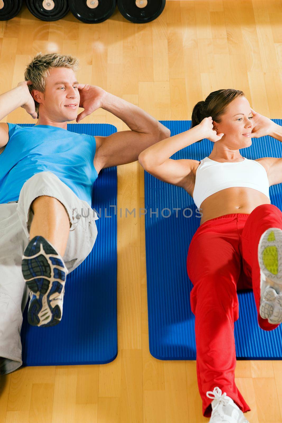 Couple with brightly colored clothes doing sit-ups in the gym
