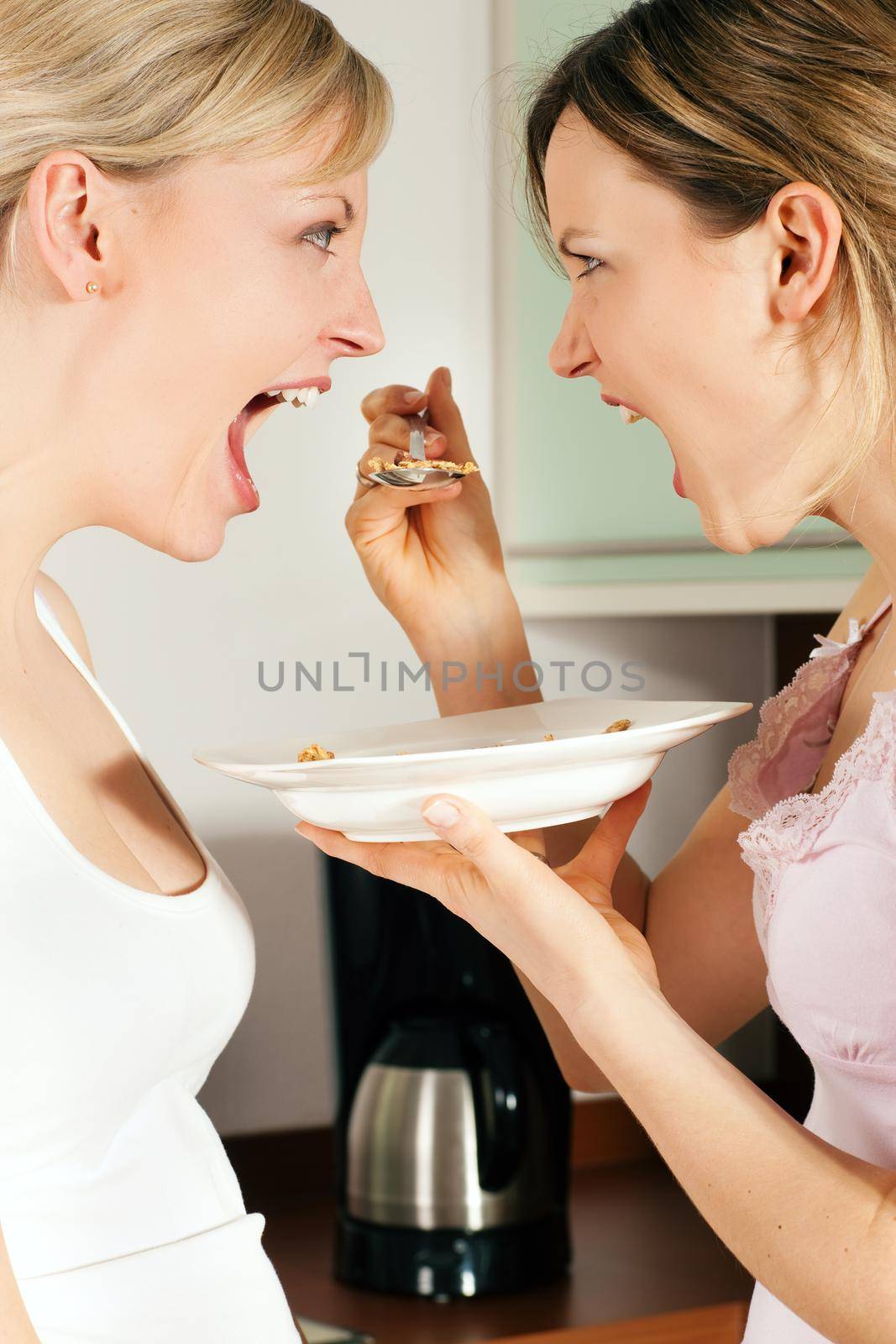 Two friends (female) having a lot of fun eating cereals for breakfast