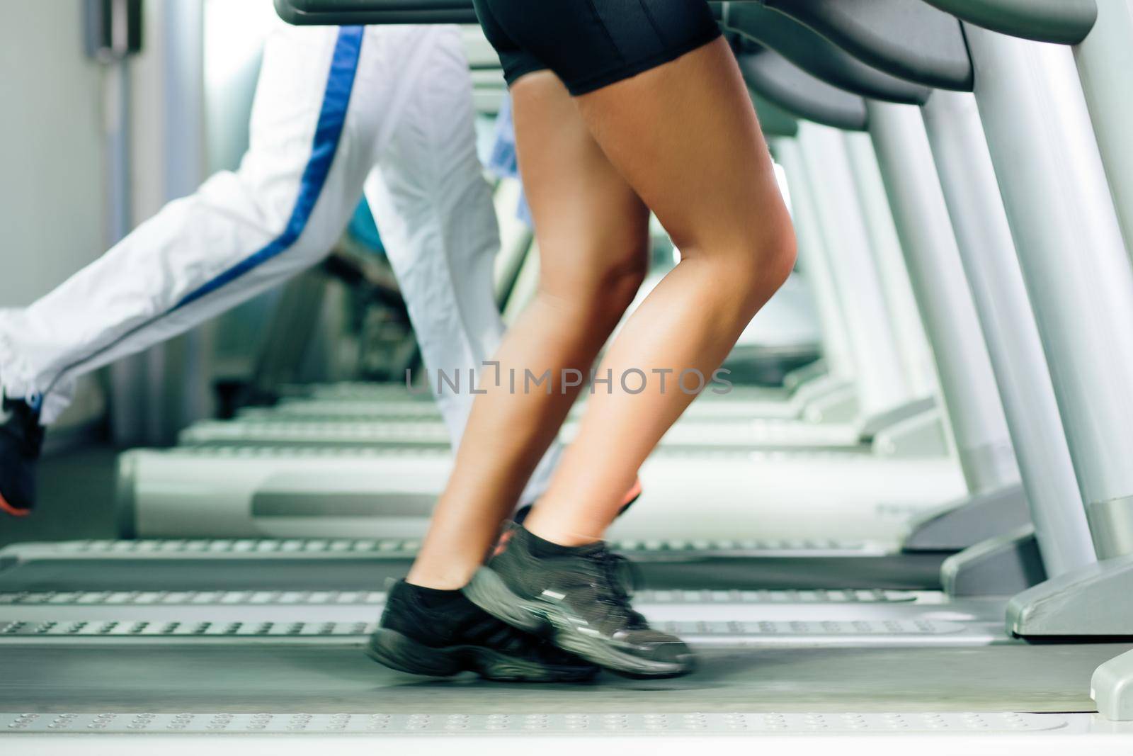 Woman and man in gym - only legs to be seen - exercising running on the treadmill to gain more fitness; motion blur in limbs for dynamic