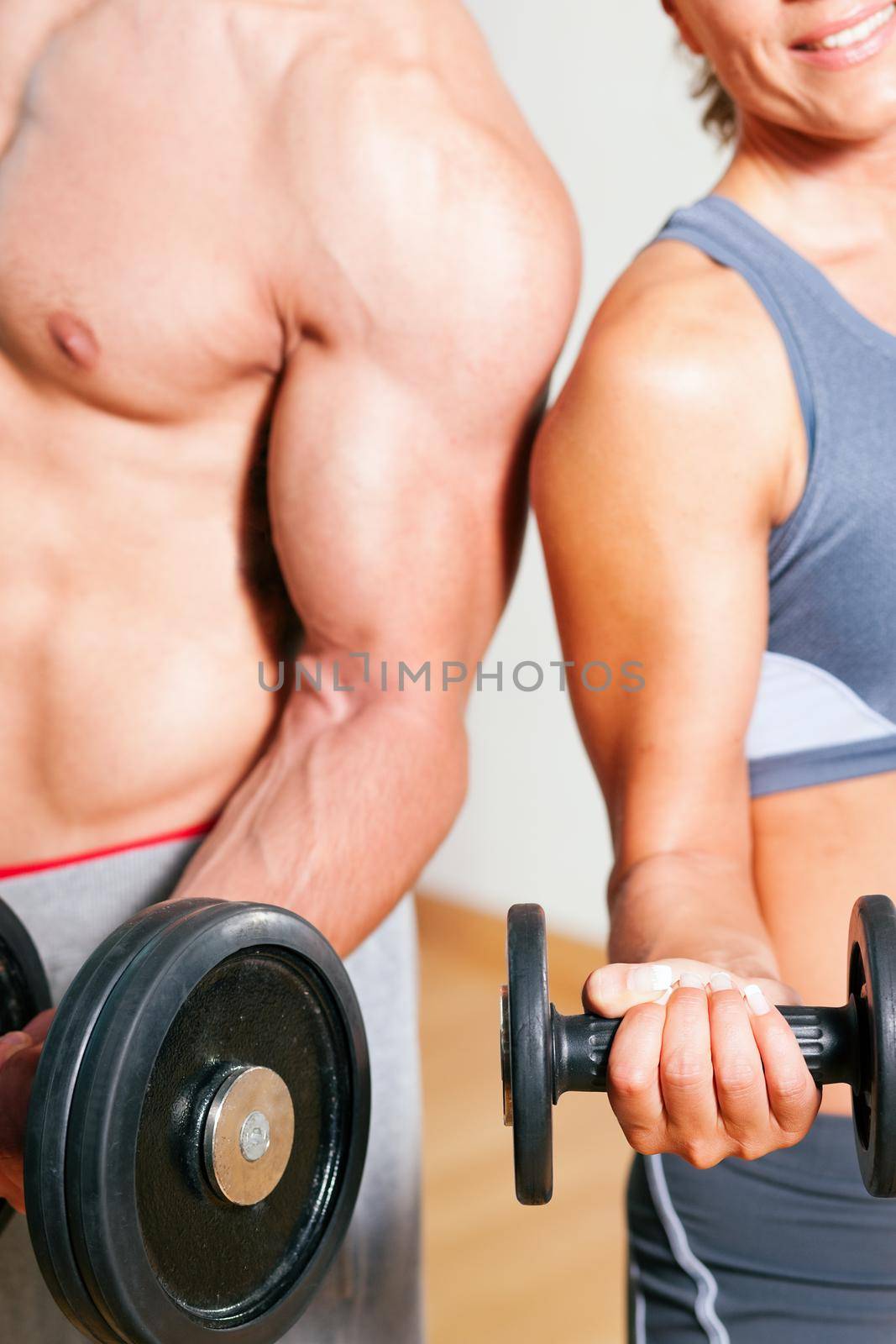 Couple exercising with dumbbells in a gym, focus on the weights, only torso of man and woman to be seen