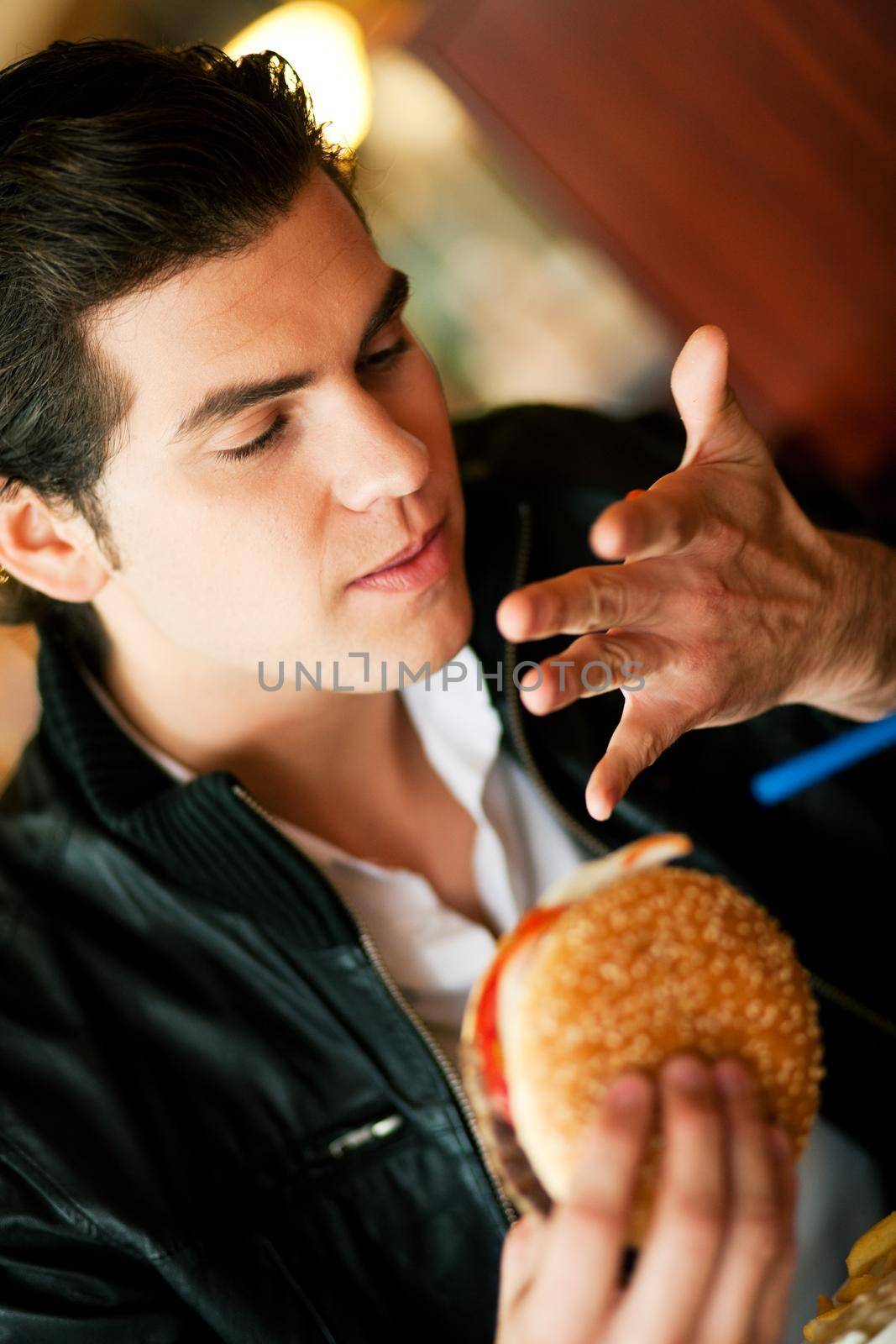 Man in a restaurant or diner eating a hamburger, it is so good he is licking his fingers, shot with available light, very selective focus
