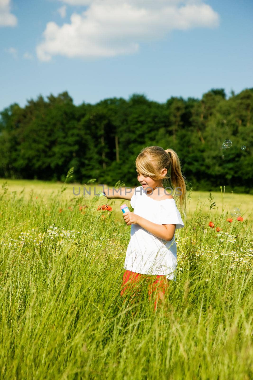 Little girl in a field making soap bubbles and having fun with it