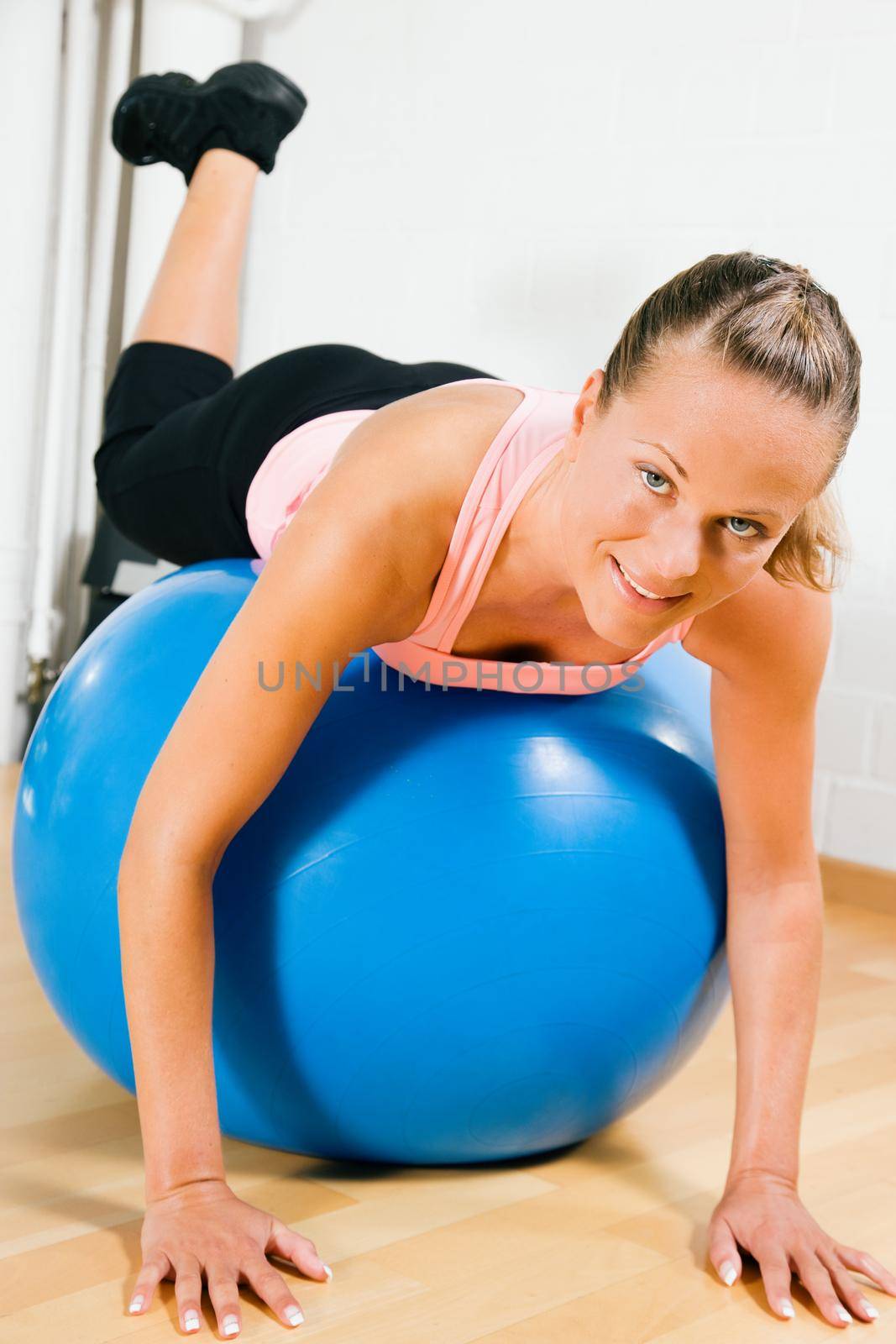 Woman leaning on top of a blue fitness ball having a break from her training looking at the viewer