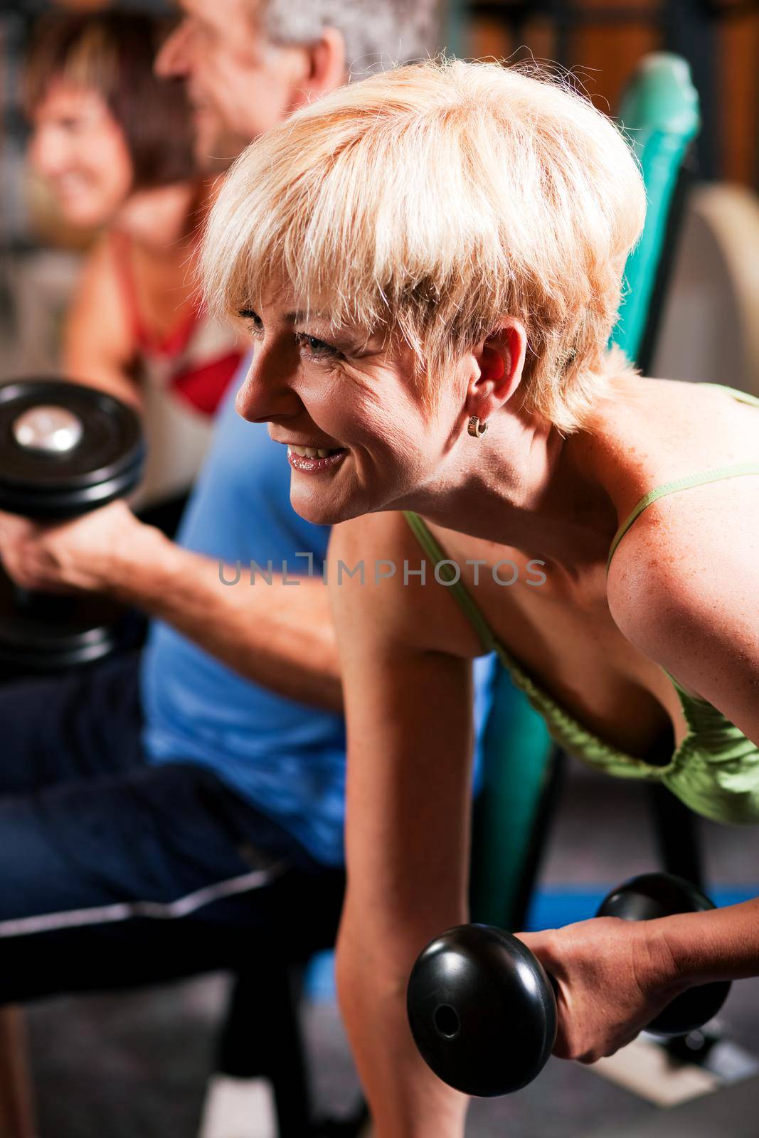 Three senior people - two women and one man - in the gym lifting dumbbells, exercising