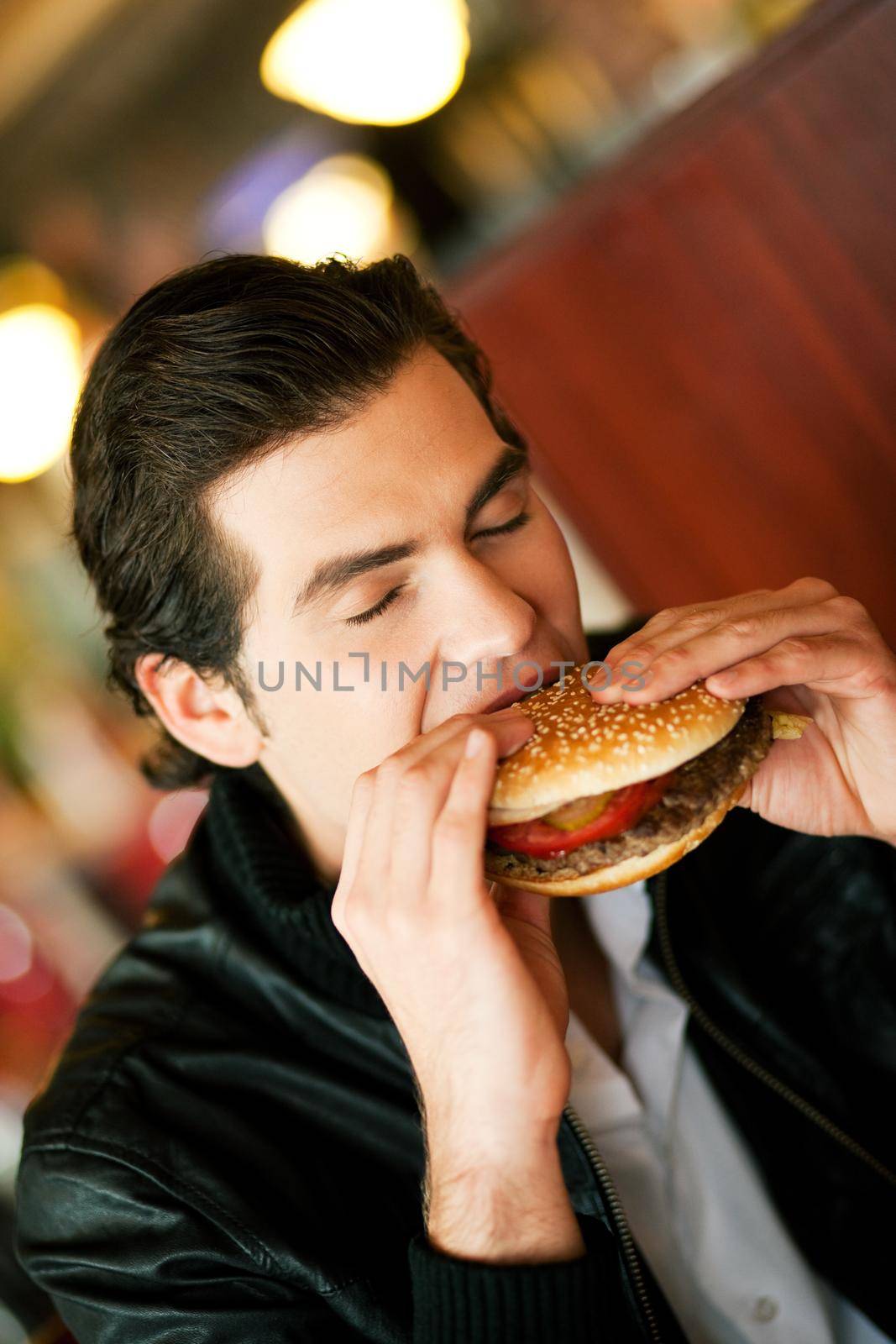 Man in a restaurant or diner eating a hamburger, he is hungry and having a good bite, shot with available light, very selective focus