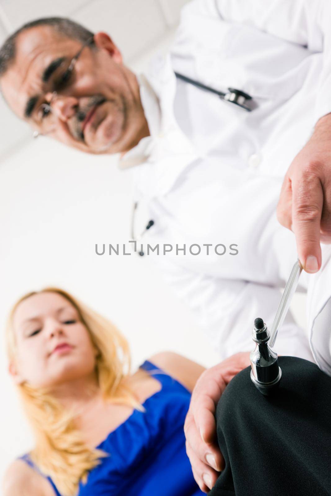 Medical doctor testing reflexes on a female patient using a little hammer